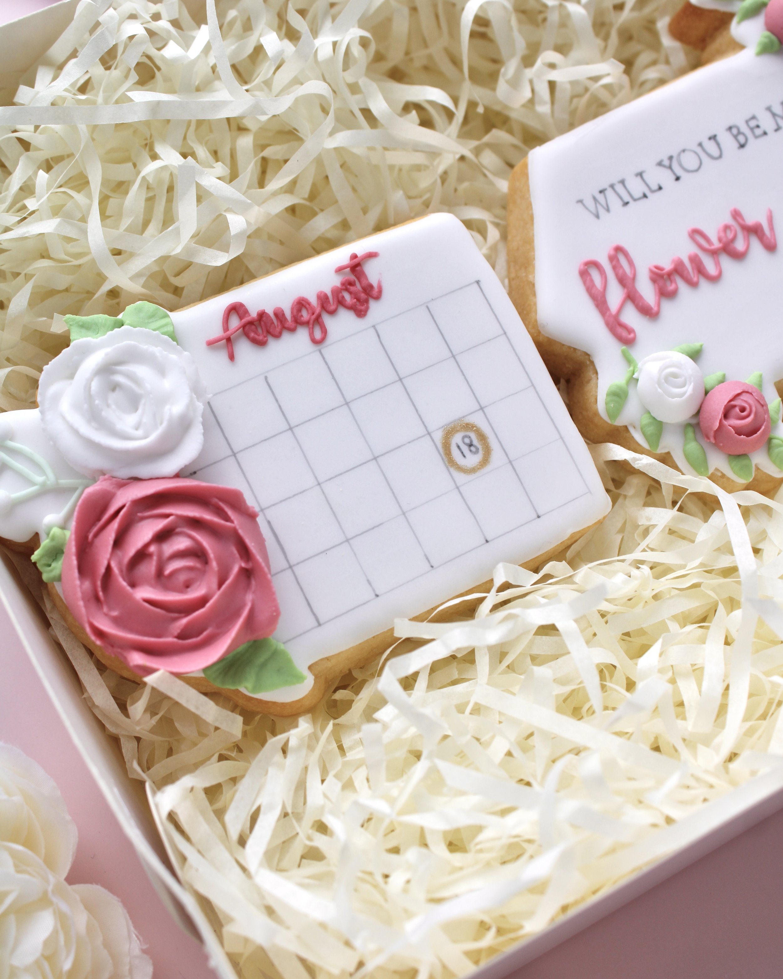 Flower girl cookie proposal box featuring three cookies, close-up of a white wedding date calendar cookie with pink and white roses.
