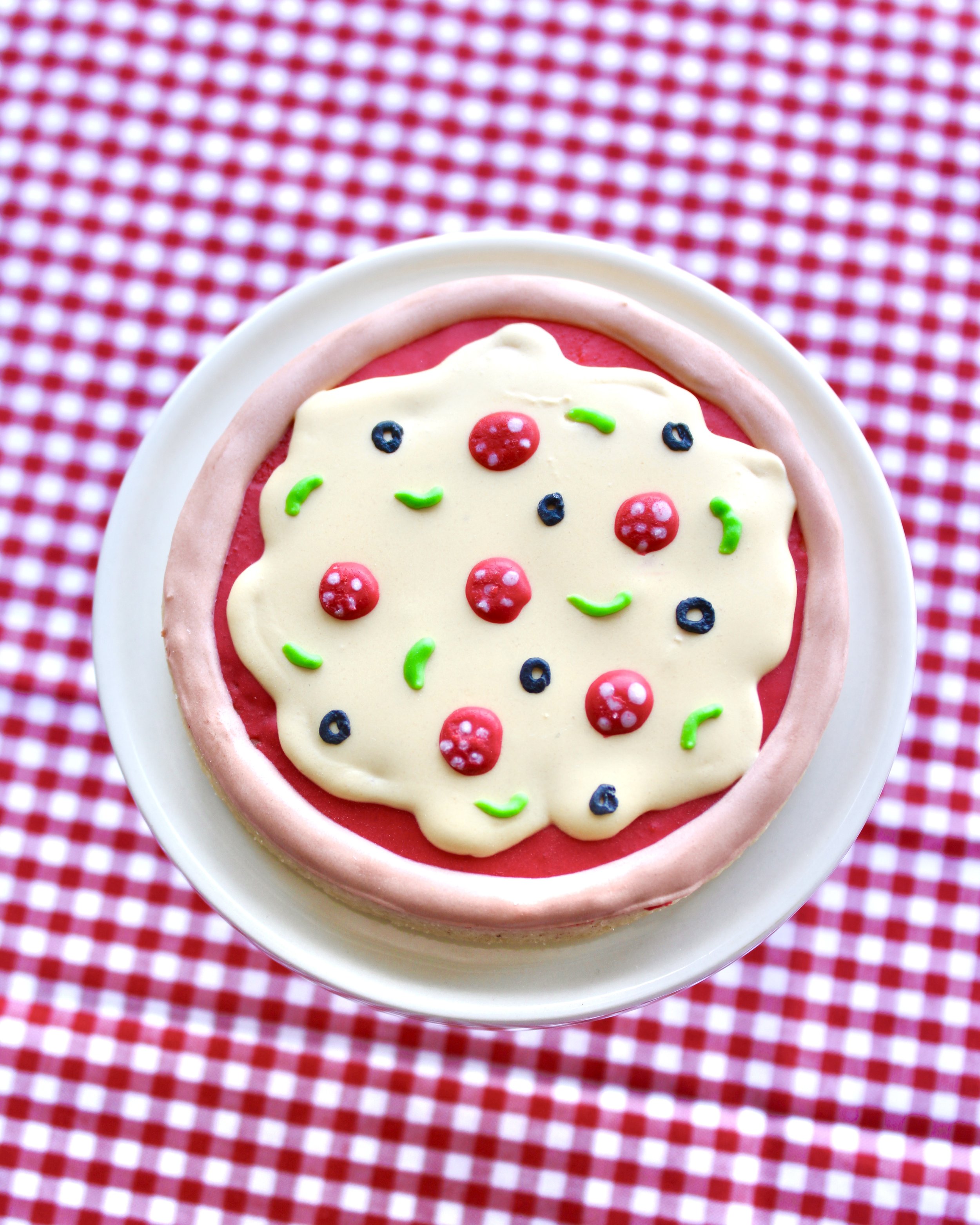Close-up of a mini pizza cookie on a mini cake stand, styled on red and white checkered fabric.