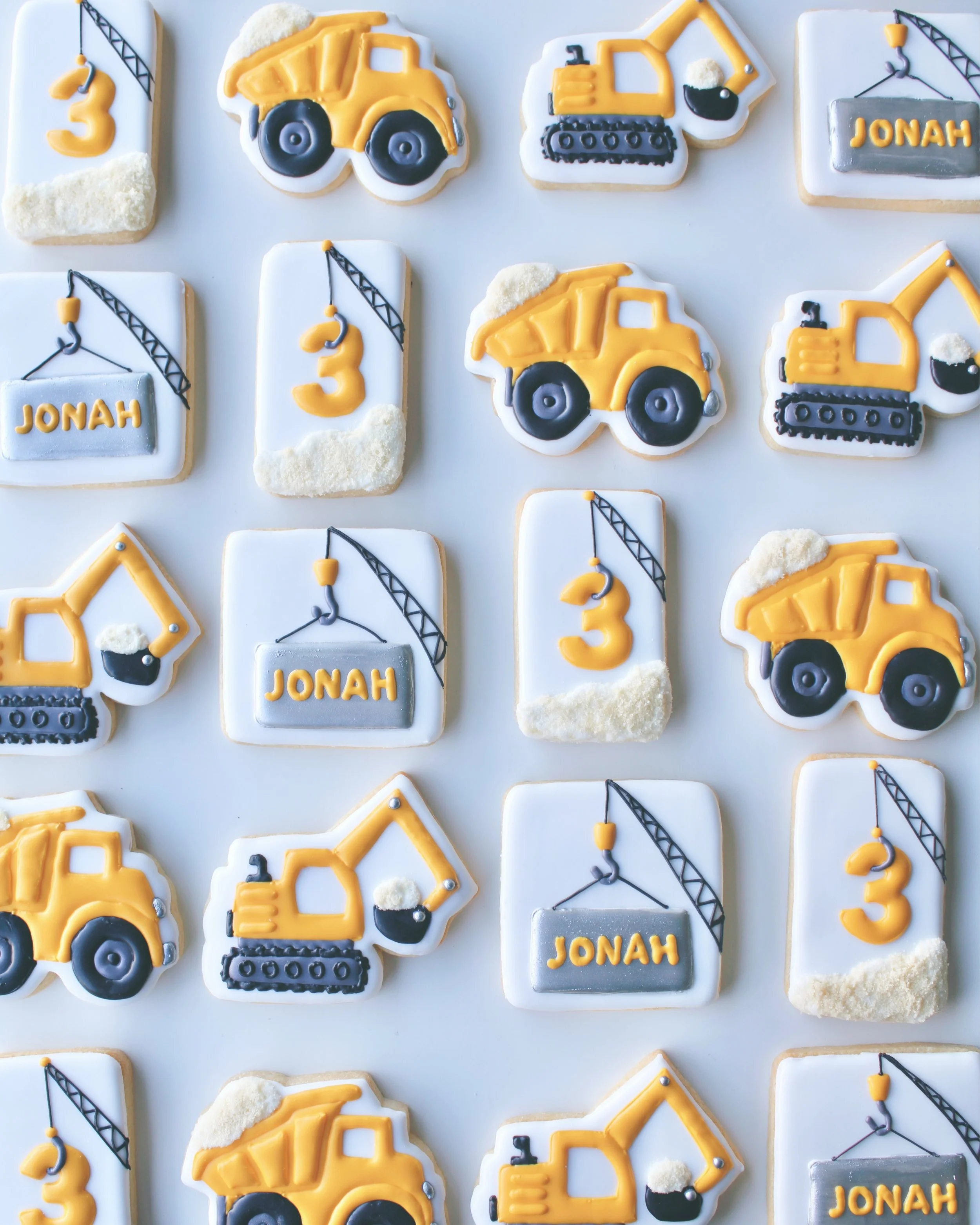 Construction Birthday Cookie Set featuring trucks, excavators and cranes in golden yellow, white, silver and black with personalised name and age cookies.