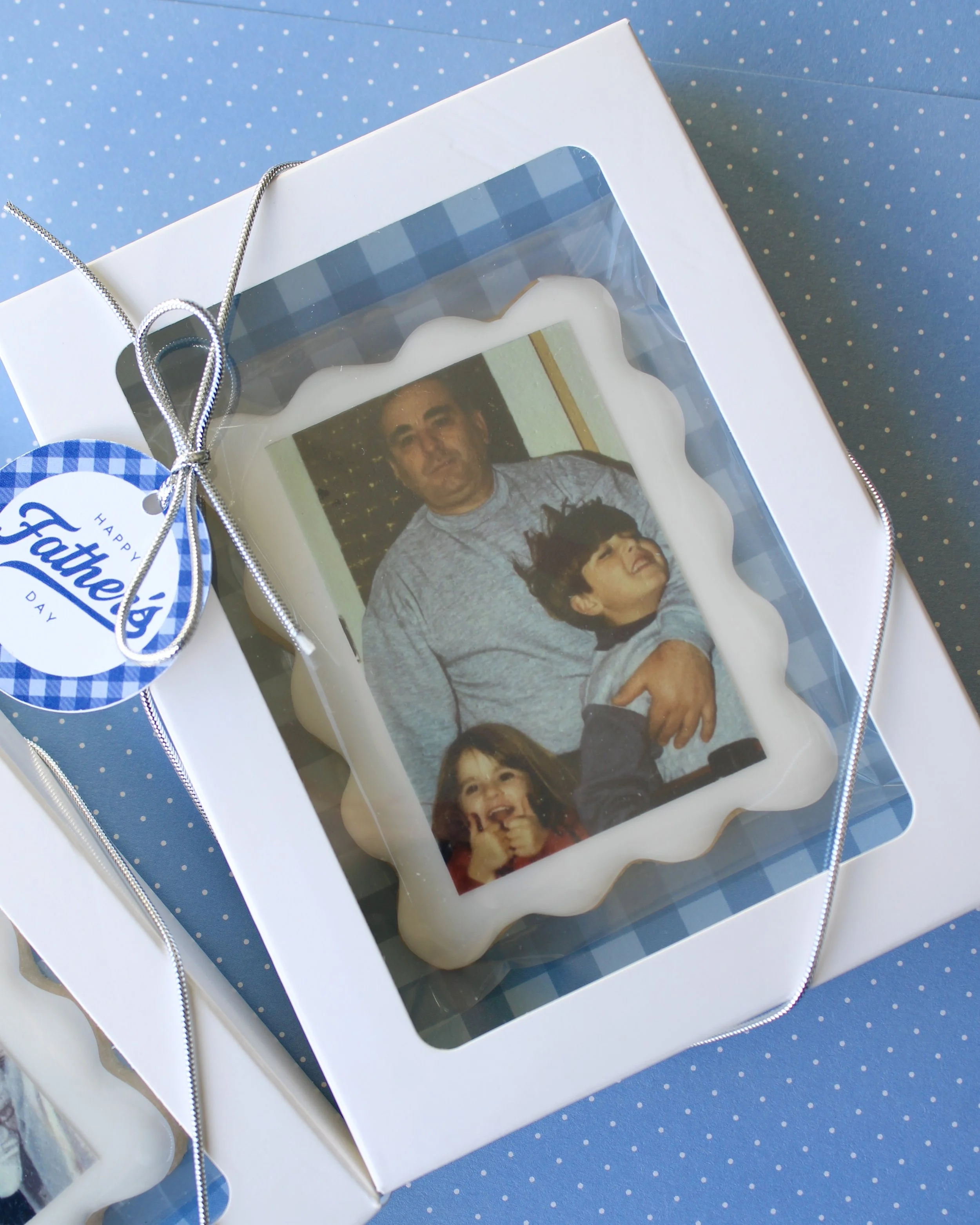 Personalised Father’s Day photo cookie gift box with white iced cookie, wavy border, printed photo, blue gingham backing, Father’s Day gift tag, and ribboned white cookie box on a blue background.