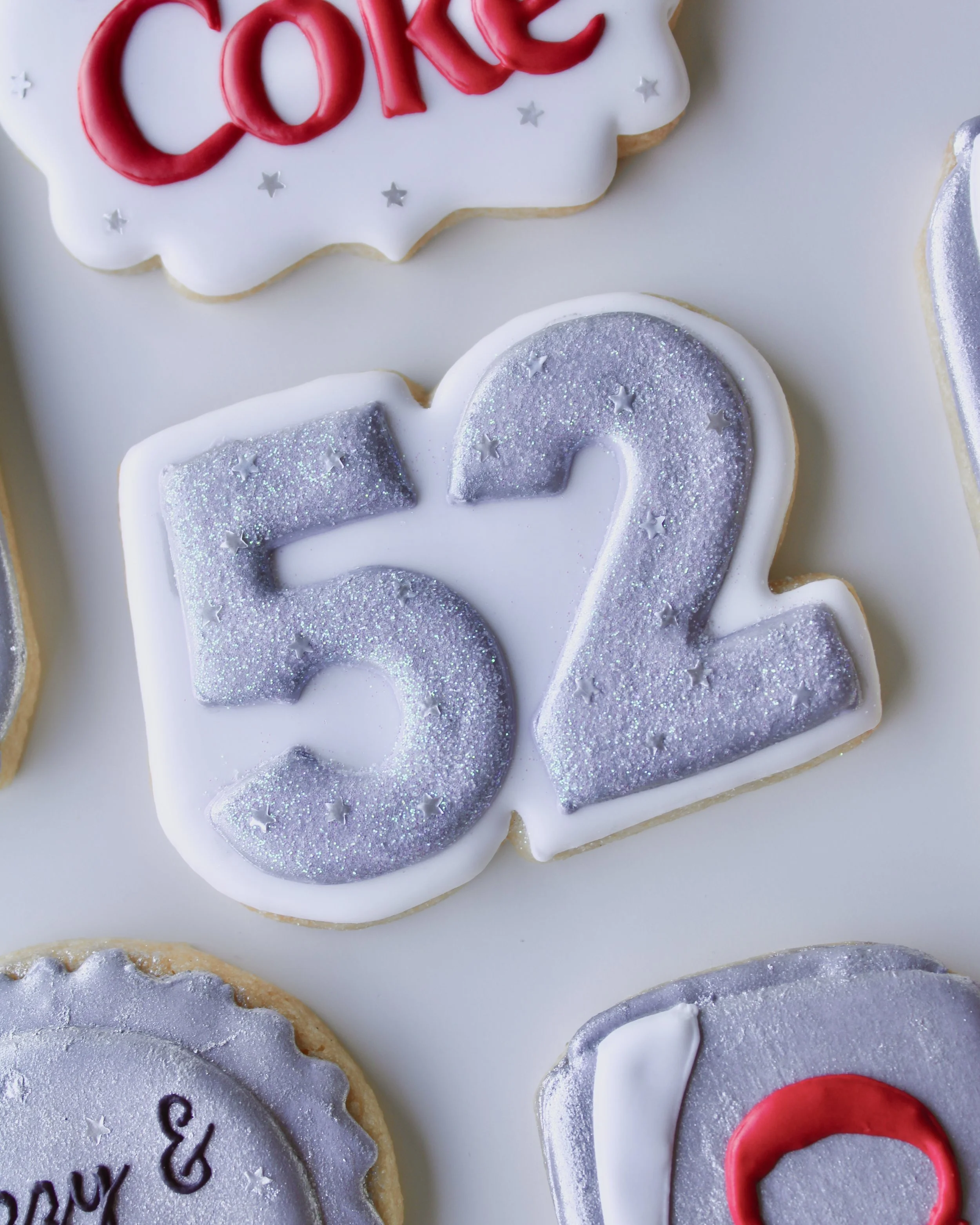 Close-up of a cookie with the number 52 in silver glitter, featuring silver star accents.