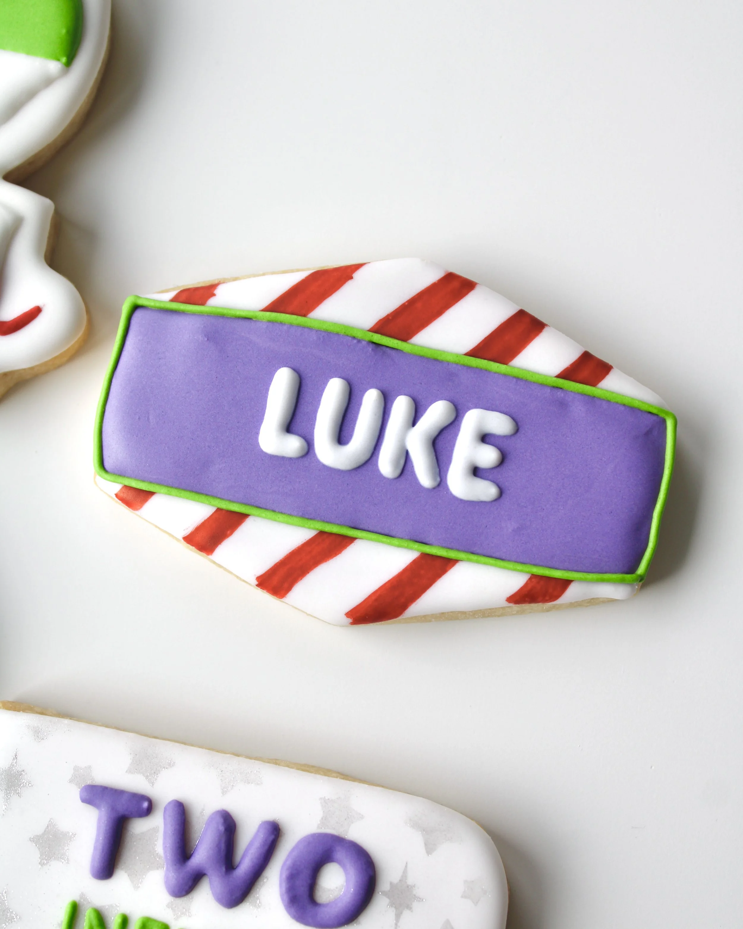 Close-up of a royal icing cookie with red stripes inspired by Buzz Lightyear’s wings and the name “Luke” in icing.