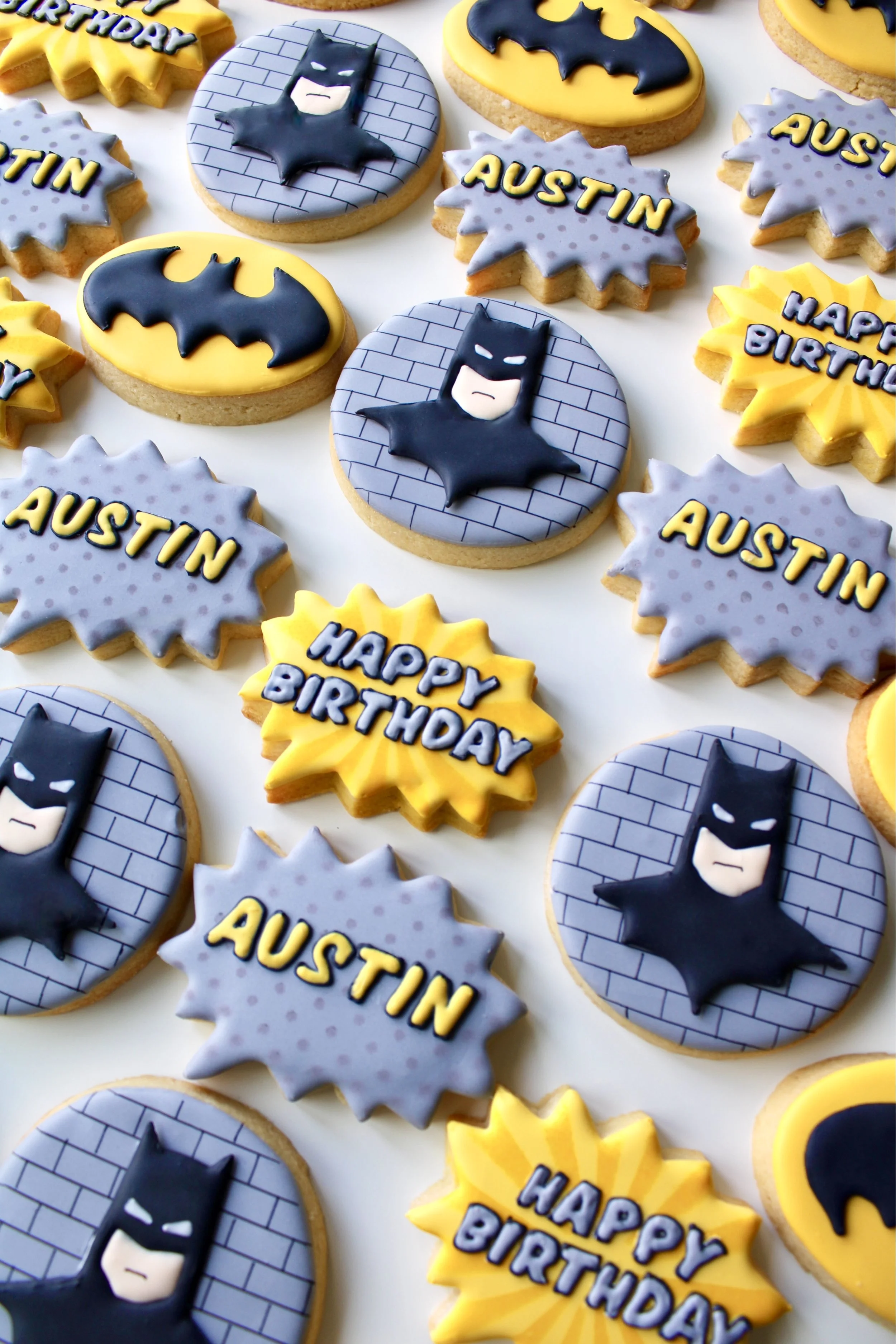Batman inspired birthday cookie set with assorted comic-style cookies in black, yellow and grey colour palette, including personalised and speech bubble designs