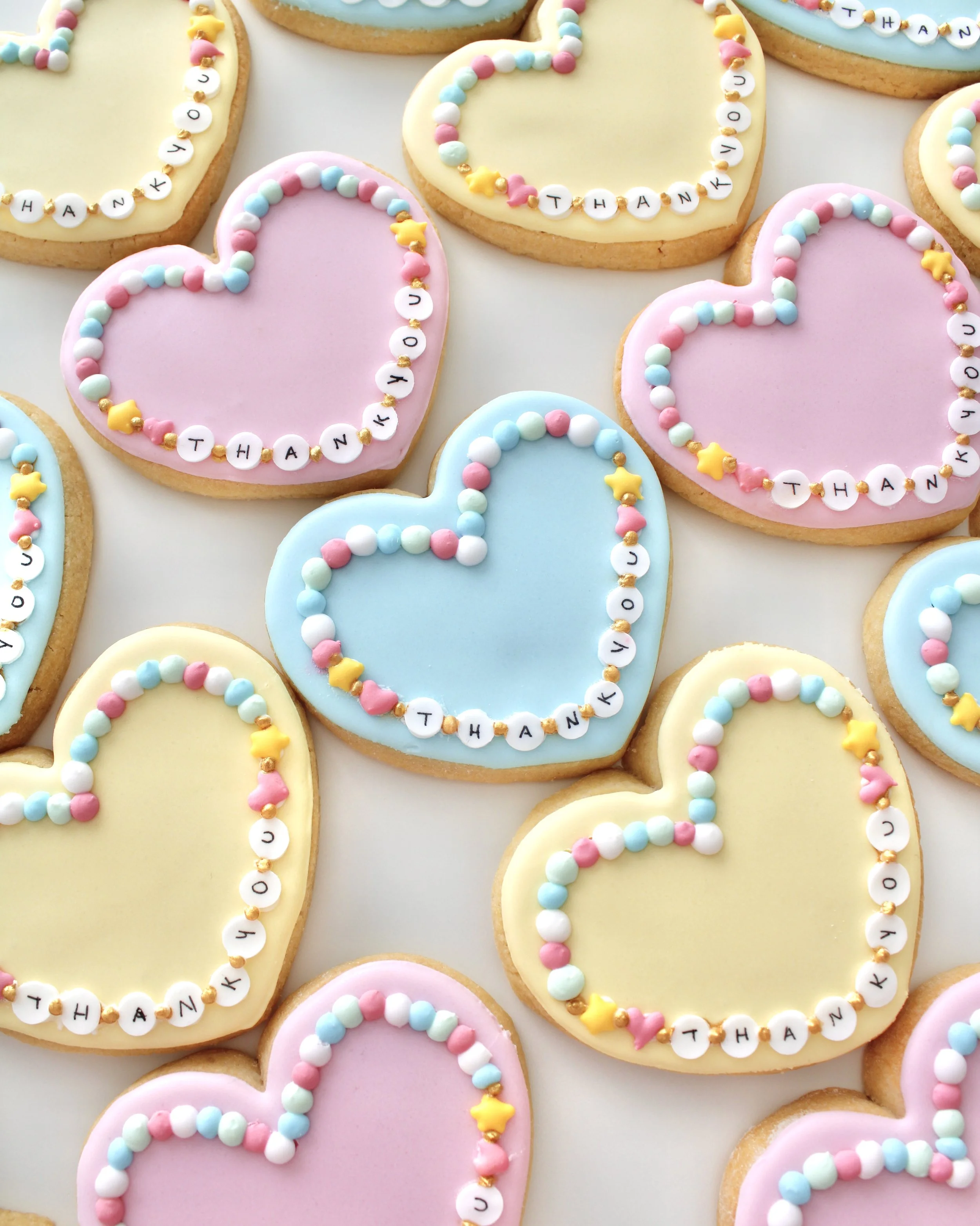 Heart-shaped friendship bracelet cookies in pastel blue, pink, and yellow.