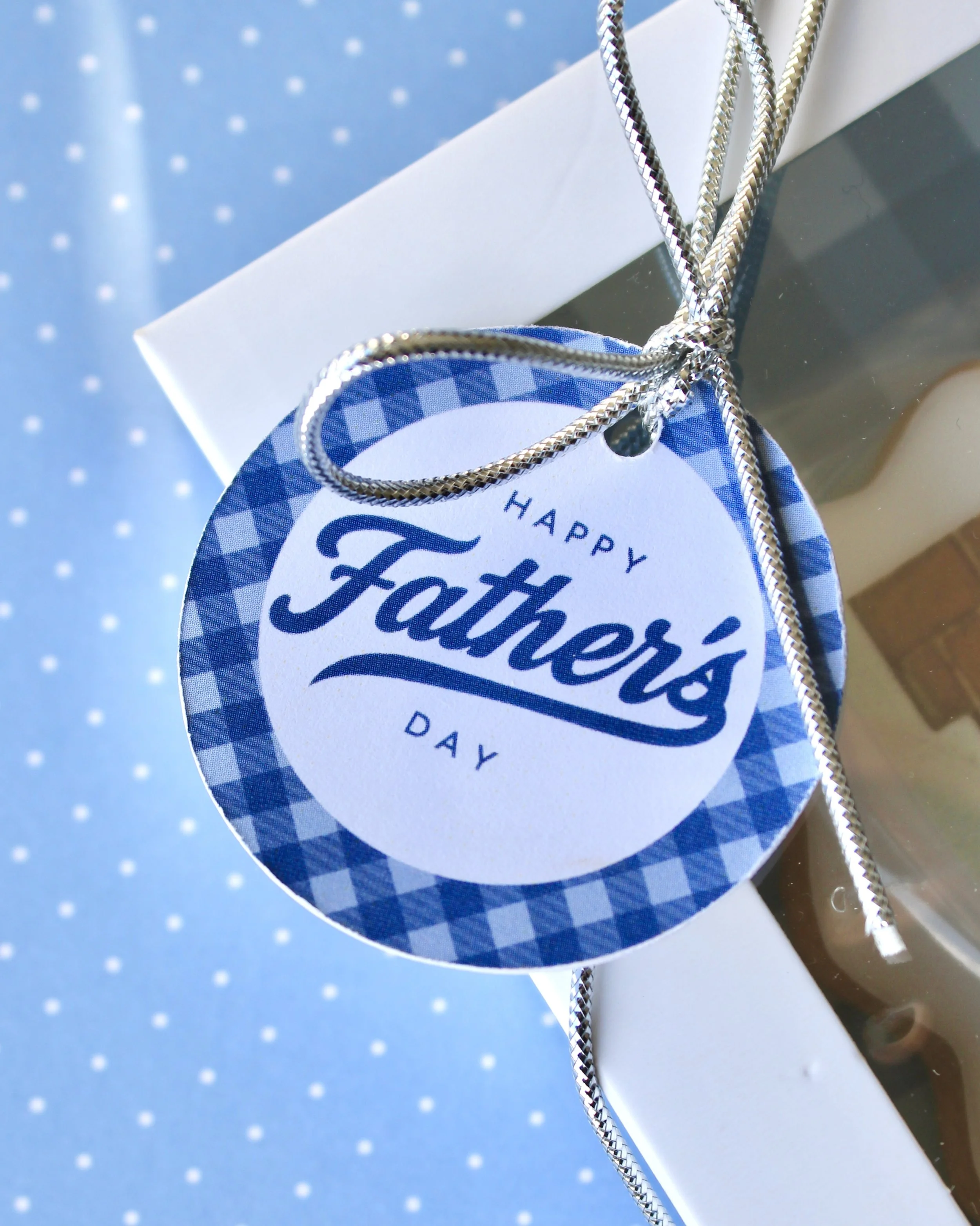Close-up of a round Father’s Day gift tag featuring “Happy Father’s Day” in blue text with a blue gingham border.