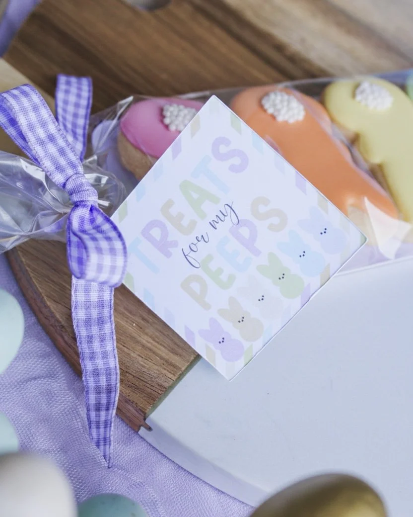 Close-up Easter gift tag reading “Treats for my Peeps” in rainbow lettering with rainbow Peeps, attached to a cookie bag with gingham bow, styled on marble and wood board.