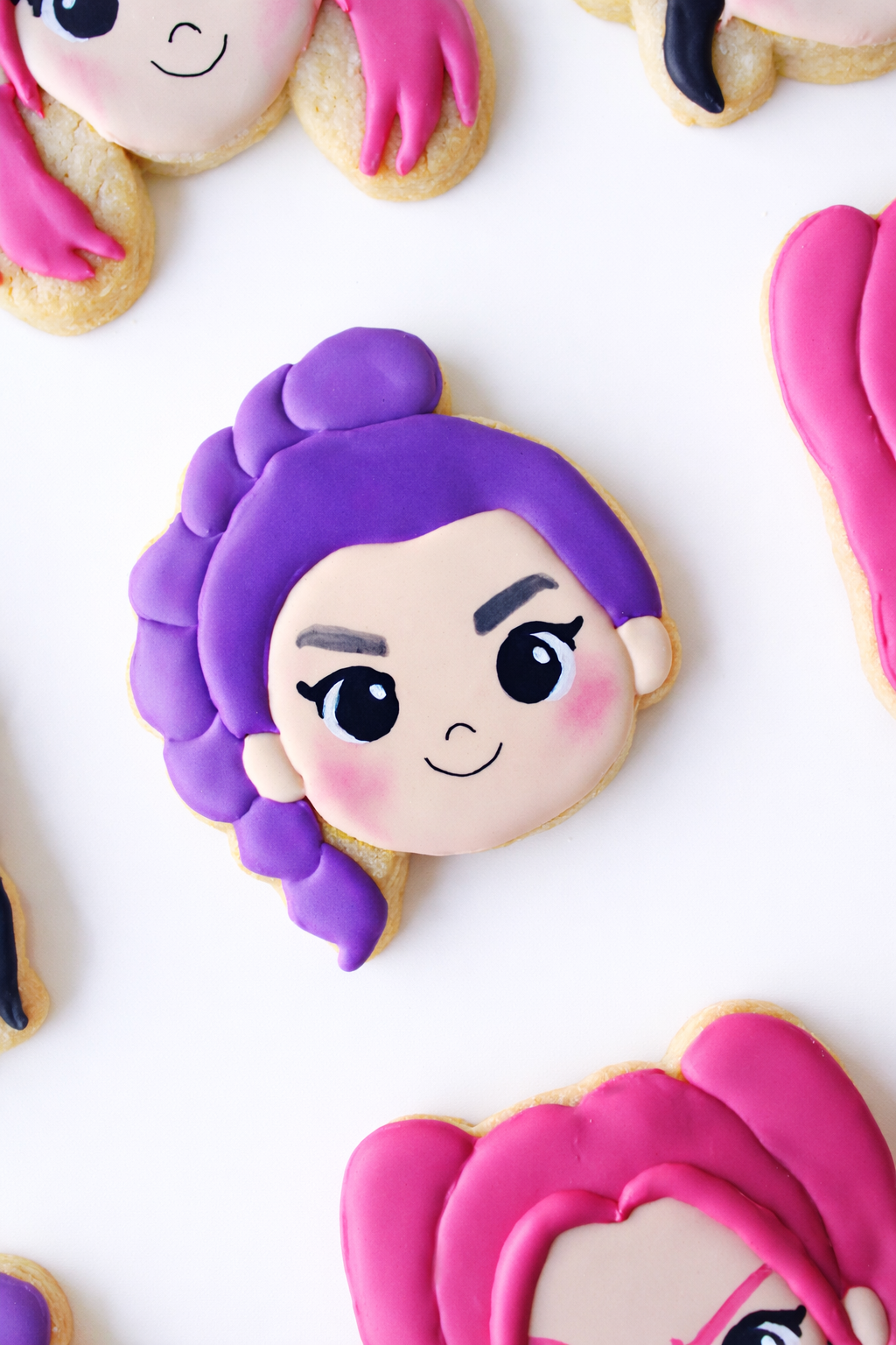 Close-up of a Demon Hunters Huntrix inspired Rumi cookie face featuring purple hair, rosy cheeks, and delicate black eyeliner makeup, with a smiling expression on a white background.