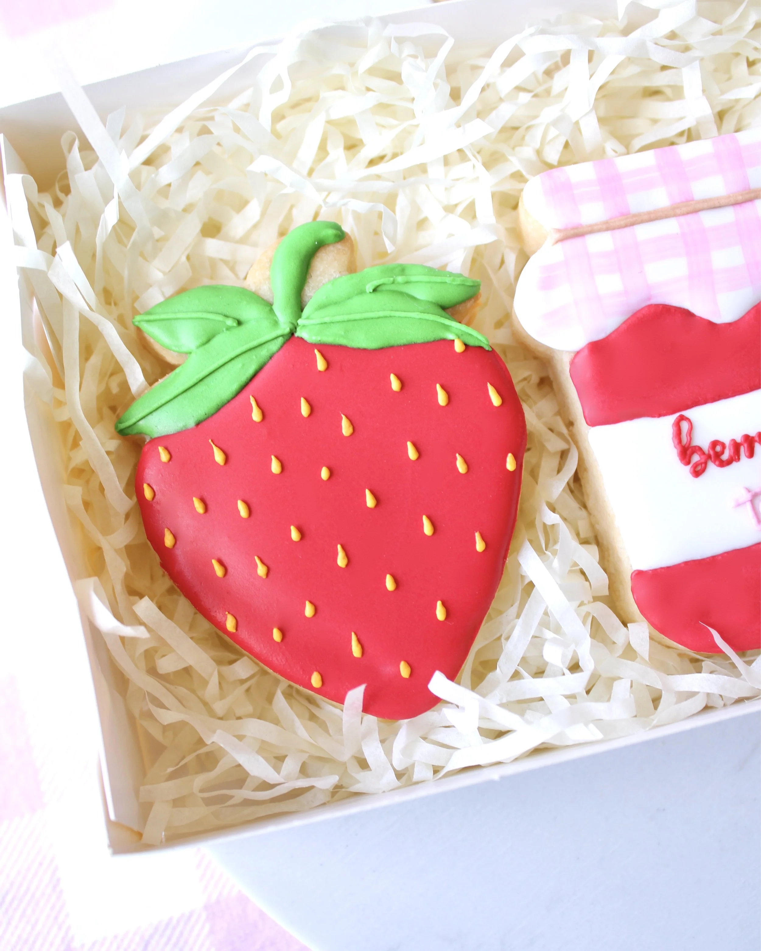 Close-up of a cookie decorated with a red royal icing strawberry featuring yellow seeds and green leaves.