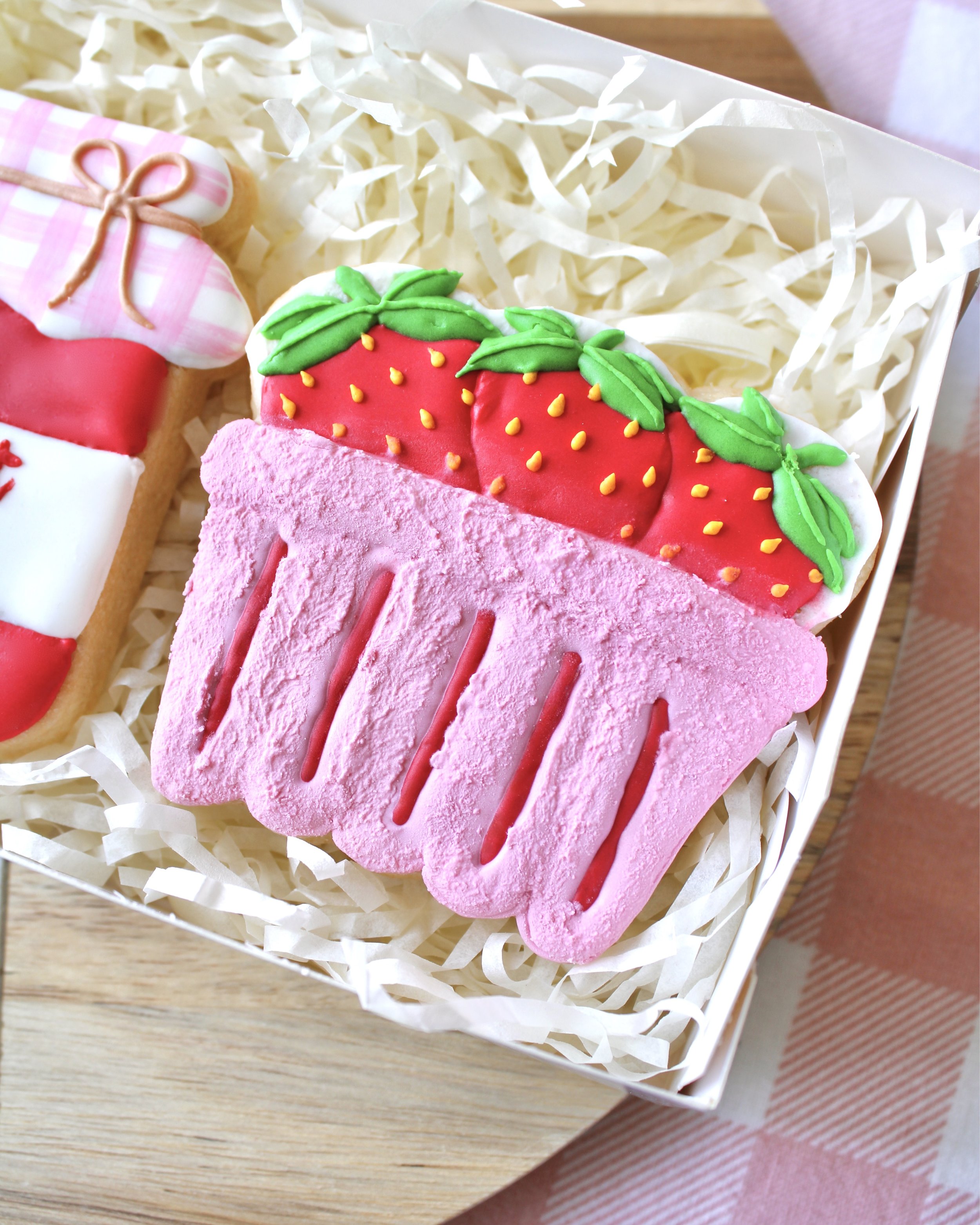 Close-up of a textured pink strawberry punnet cookie decorated with three royal icing strawberries with yellow seeds and green leaves.
