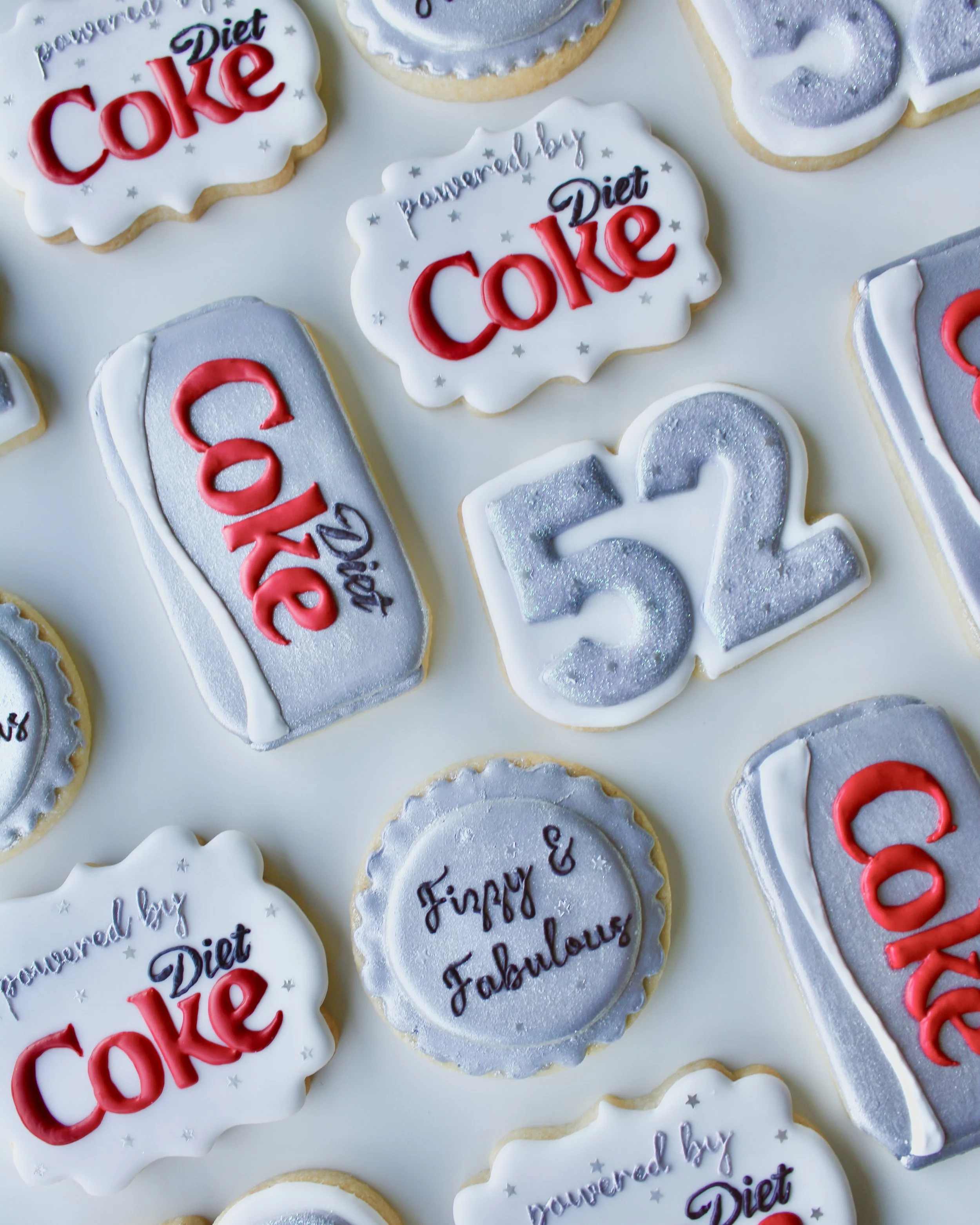 Diet Coke themed birthday cookies in silver, white and red accents, featuring Diet Coke cans and bottle cap designs.