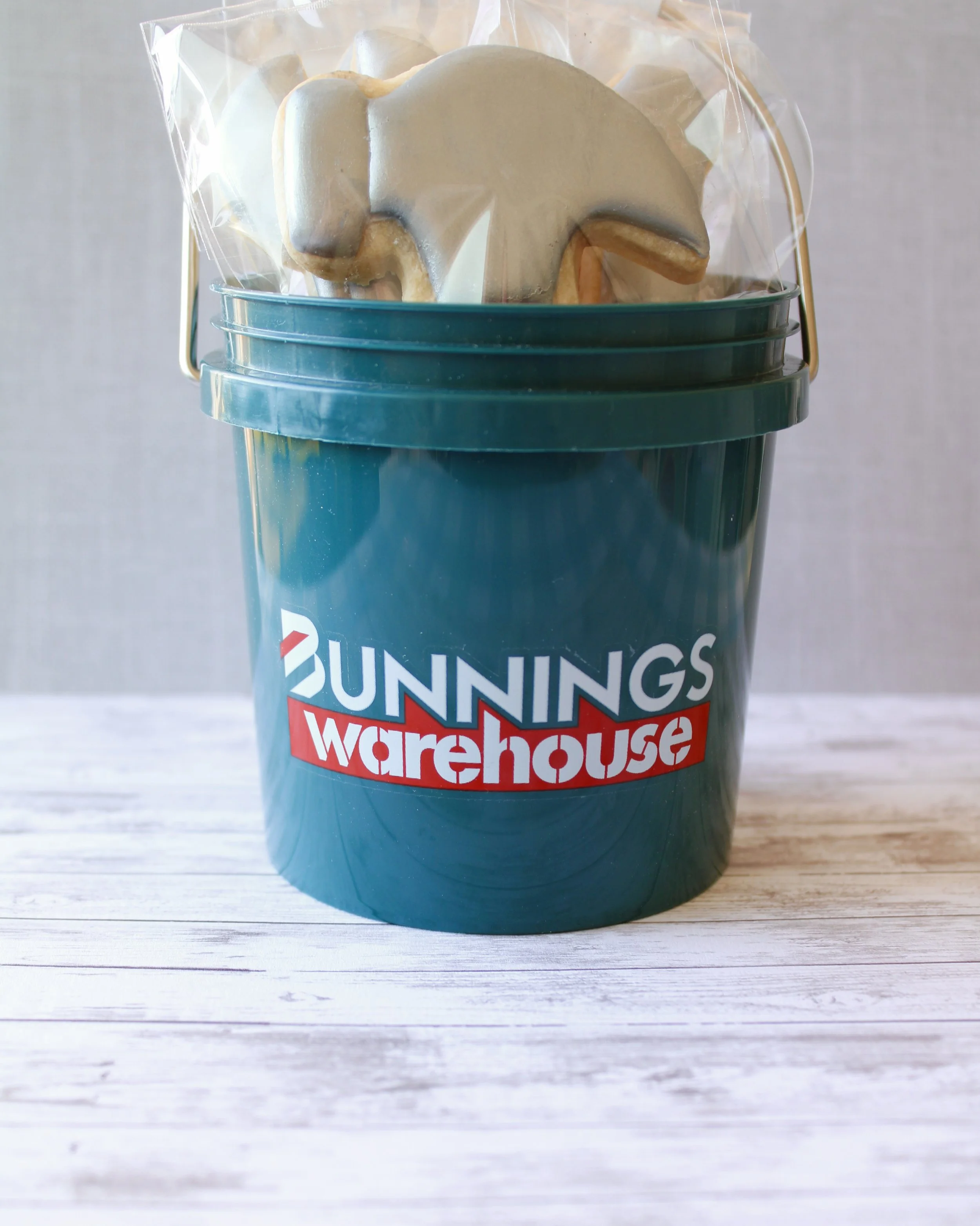 Father's Day tool cookies decorated in silver and red icing, presented in a dark green Bunnings Warehouse mini bucket, styled on a grey washed wooden background.