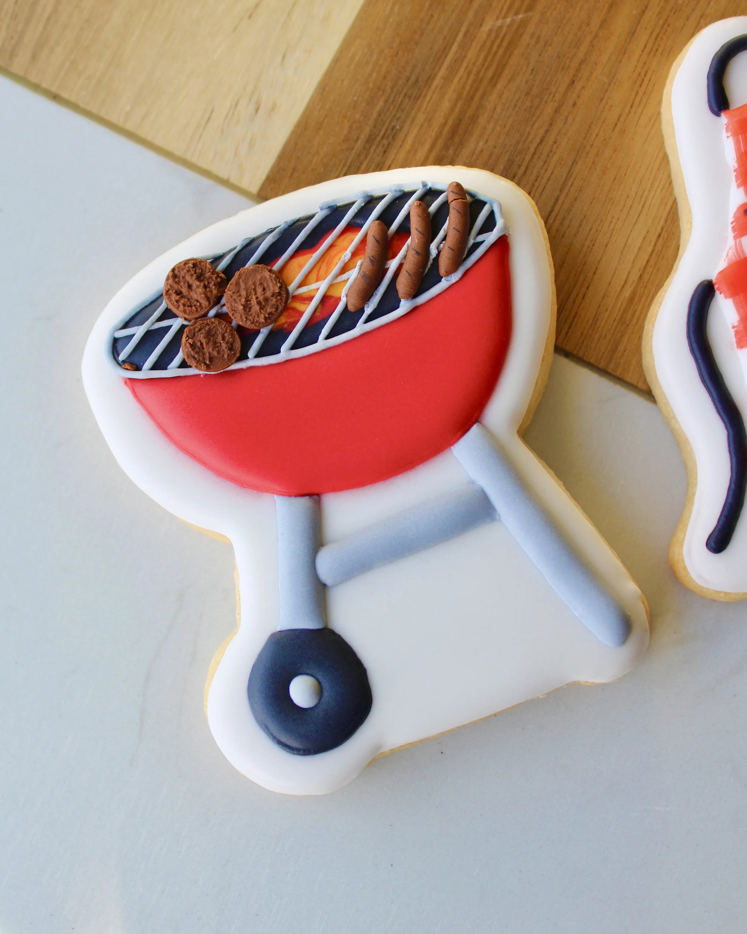 Close up of Father's Day cookie featuring a red BBQ with meats on it, styled on a wooden board.