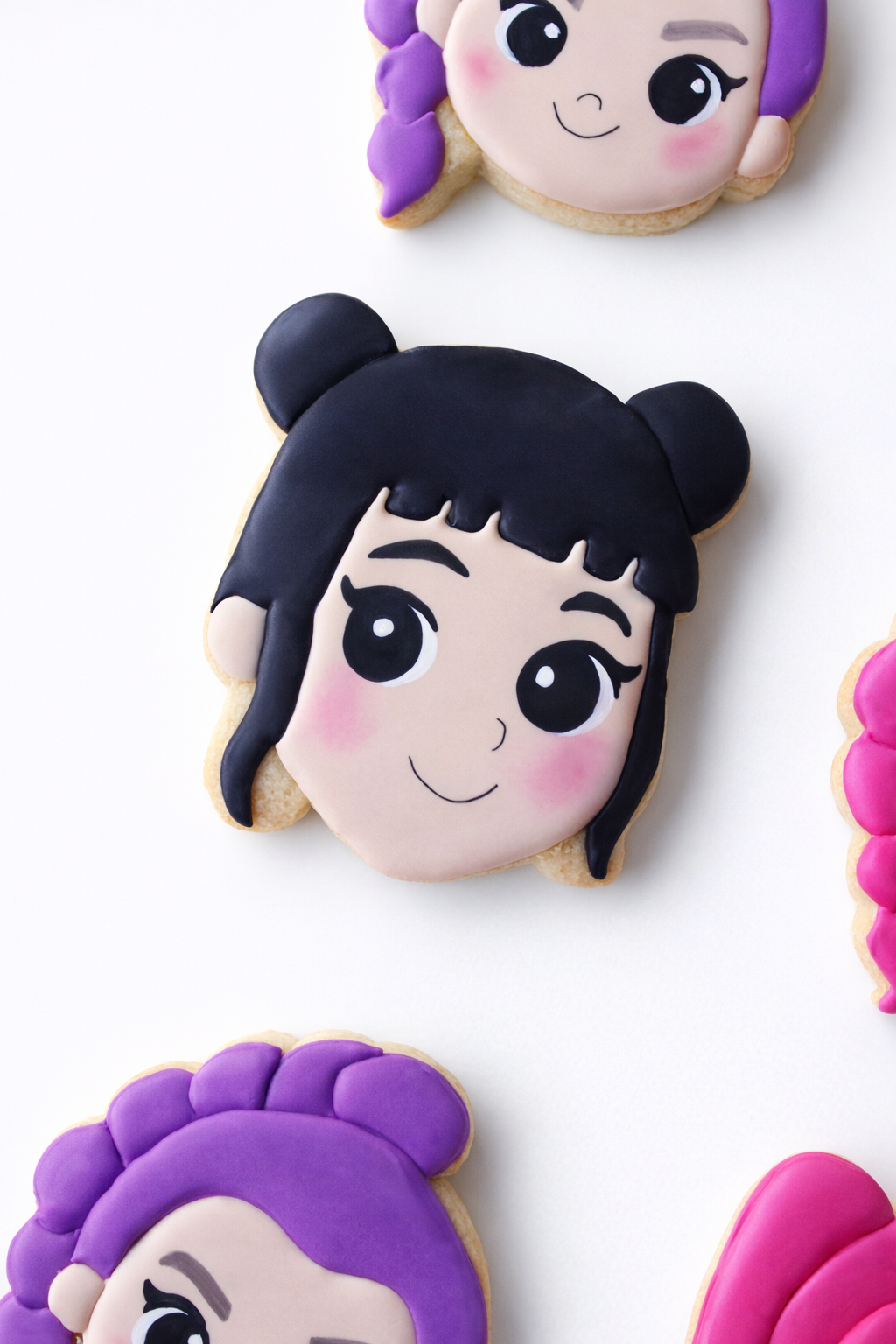 Close-up of a Demon Hunters Huntrix inspired Zooey cookie face featuring black hair, rosy cheeks, and delicate black eyeliner makeup, with a smiling expression on a white background.