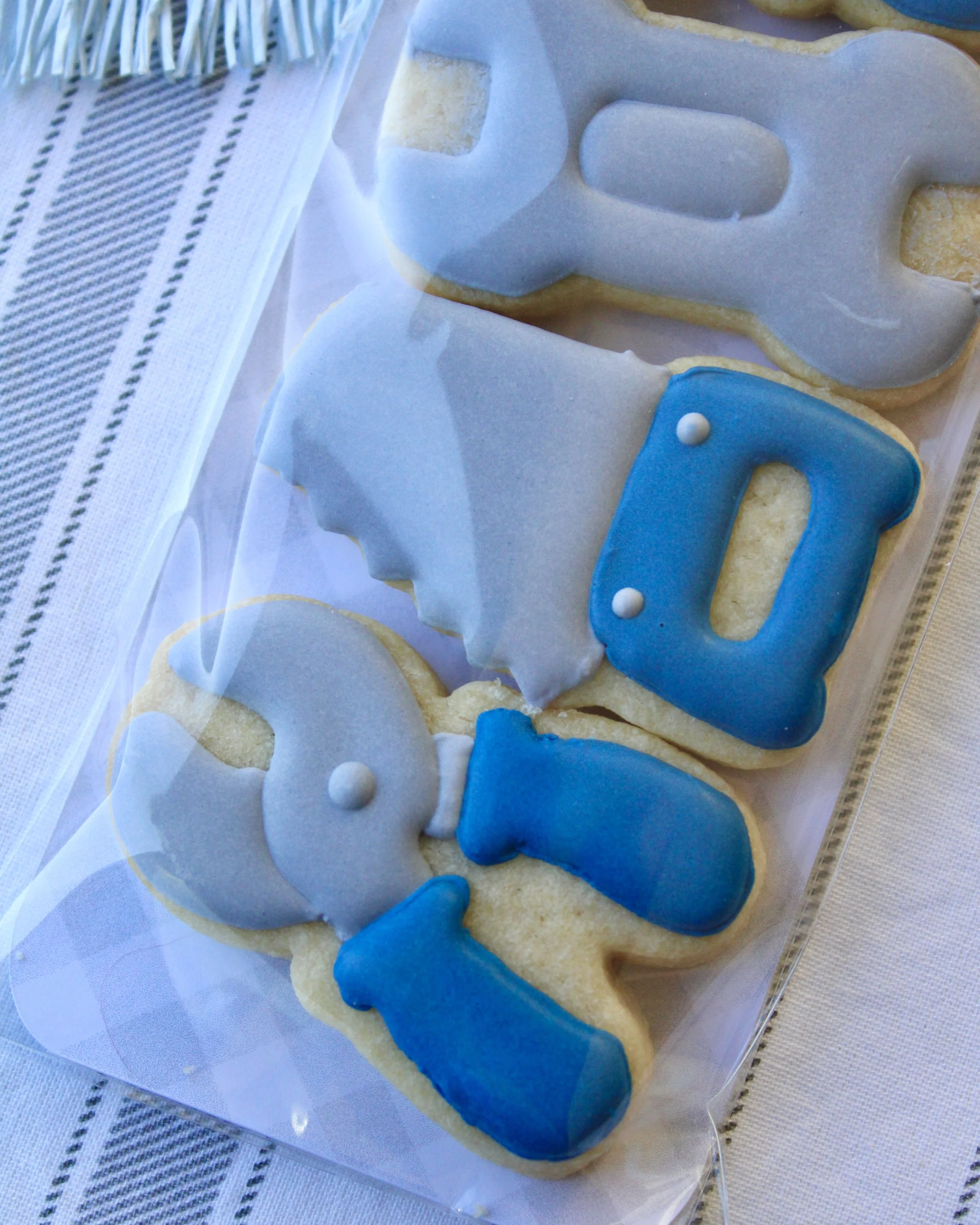 Father’s Day cookie pack with mini tool-shaped sugar cookies including a hammer, screwdriver, wrench, saw and pliers in grey and blue, packaged with a white bow and Happy Father’s Day gift tag.