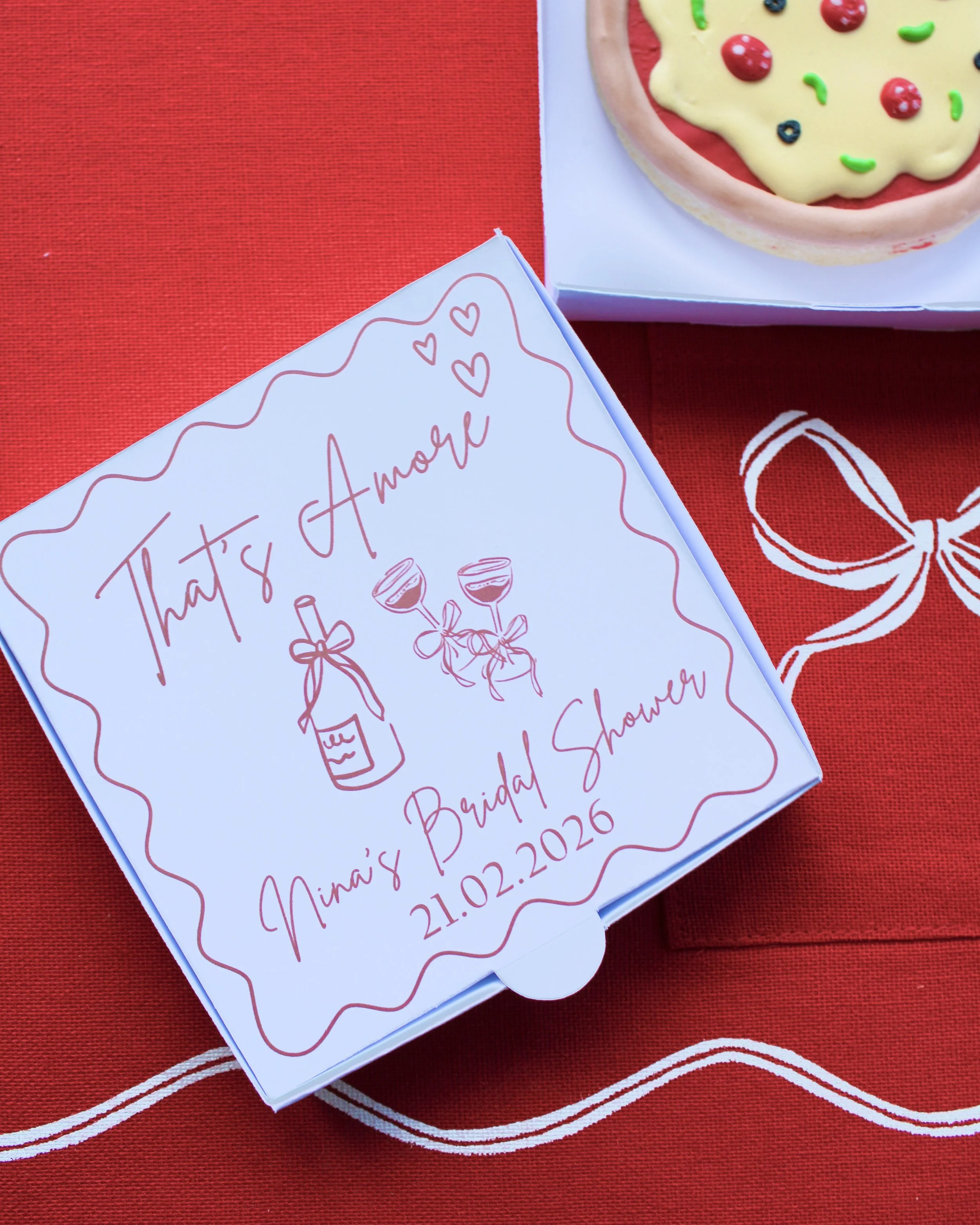Mini pizza box reading “That’s Amore” with the couple’s names and wedding date, styled on red fabric.