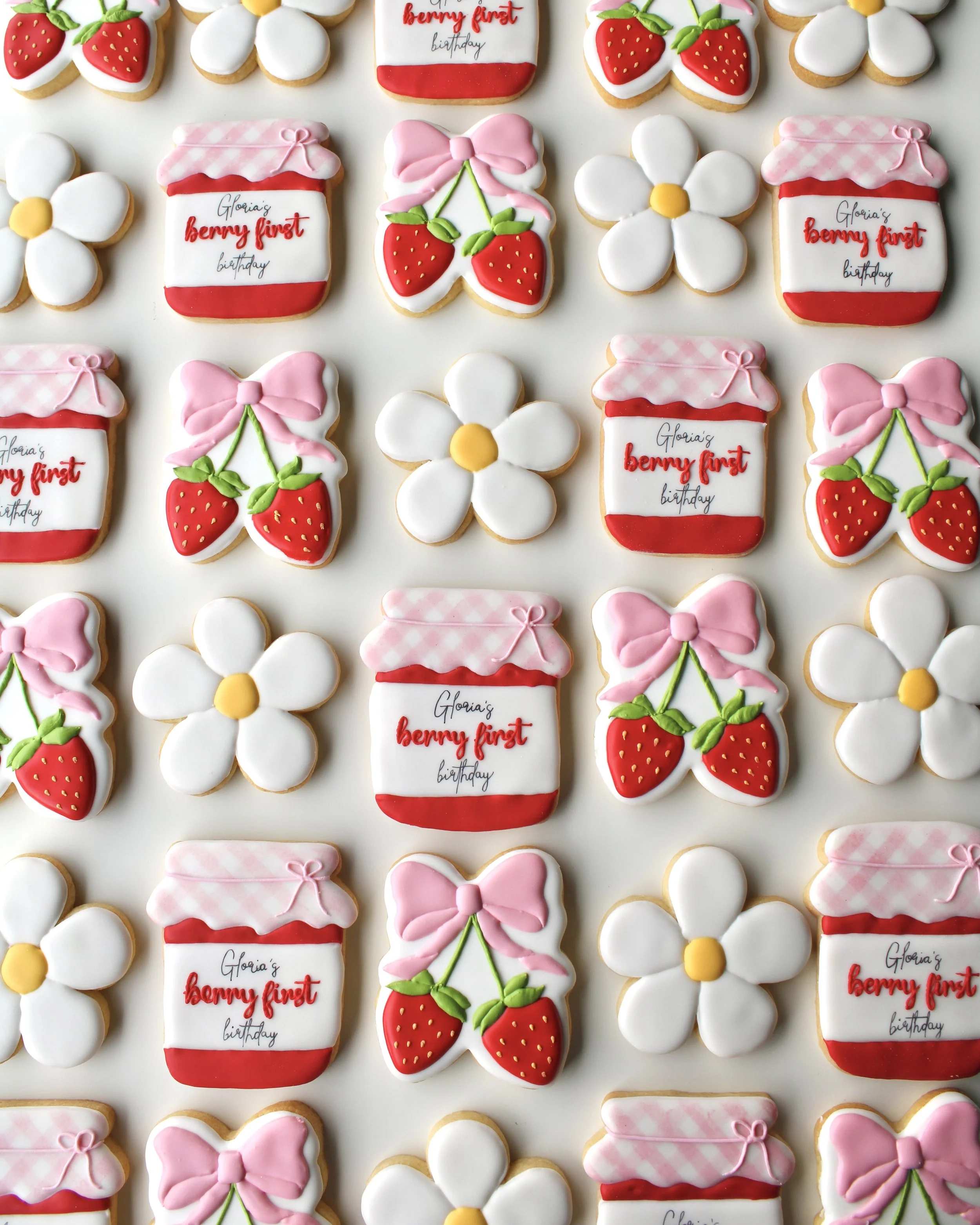 Decorated cookies with birthday theme including strawberries, daisies, and pink bows, with some cookies having the text "Gloria's berry first birthday."