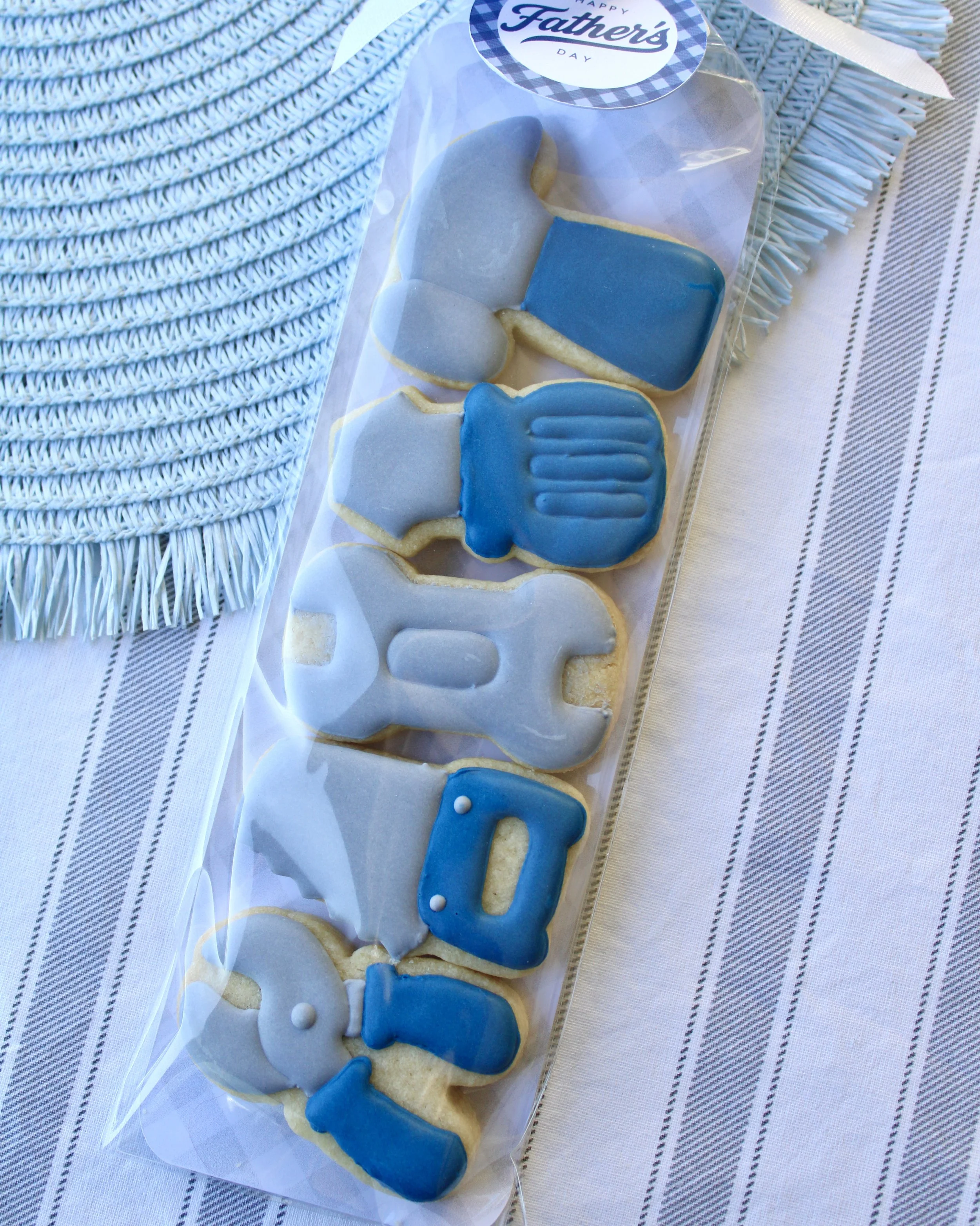 Father’s Day cookie pack with mini tool-shaped sugar cookies including a hammer, screwdriver, wrench, saw and pliers in grey and blue, packaged with a white bow and Happy Father’s Day gift tag.