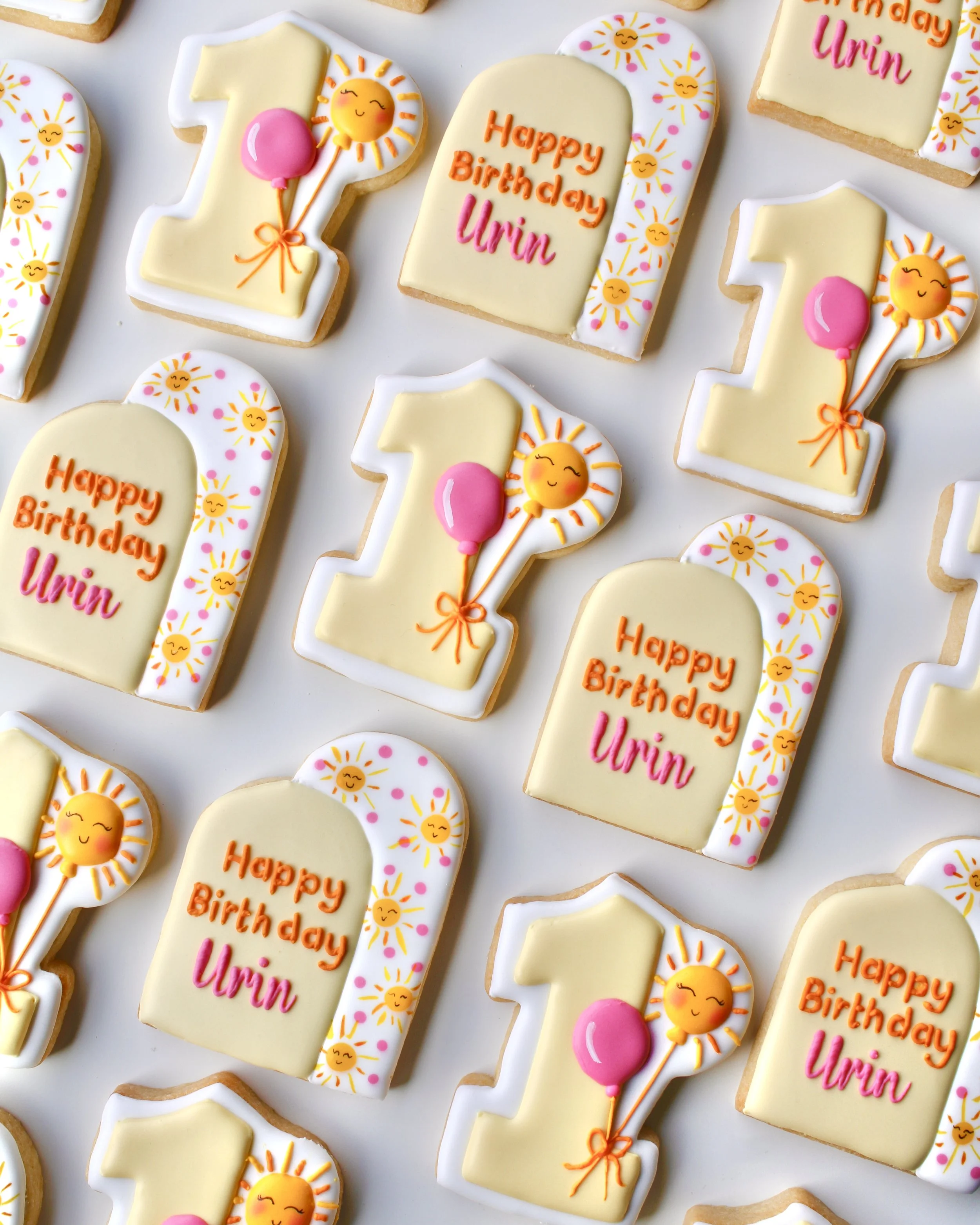 Sunny One themed birthday cookies featuring pale and bright yellows, white, hot pink and orange accents, with double arch designs, hand-painted suns and a number 1 cookie with balloon details.