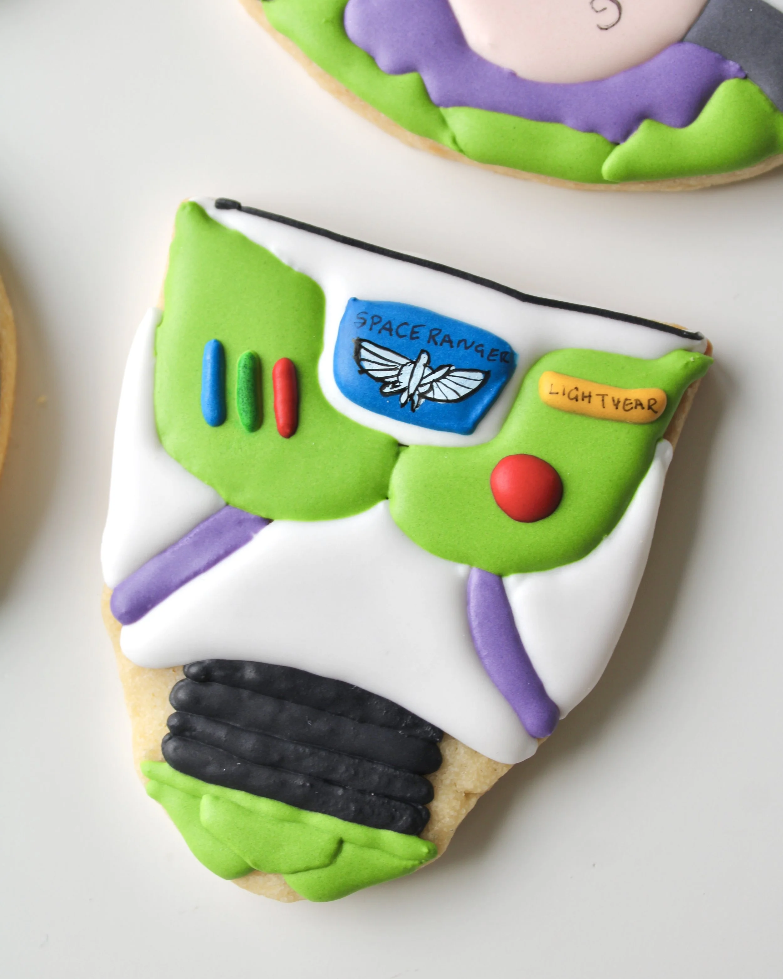 Close-up of a royal icing cookie decorated like Buzz Lightyear’s space suit in white, green and purple icing.