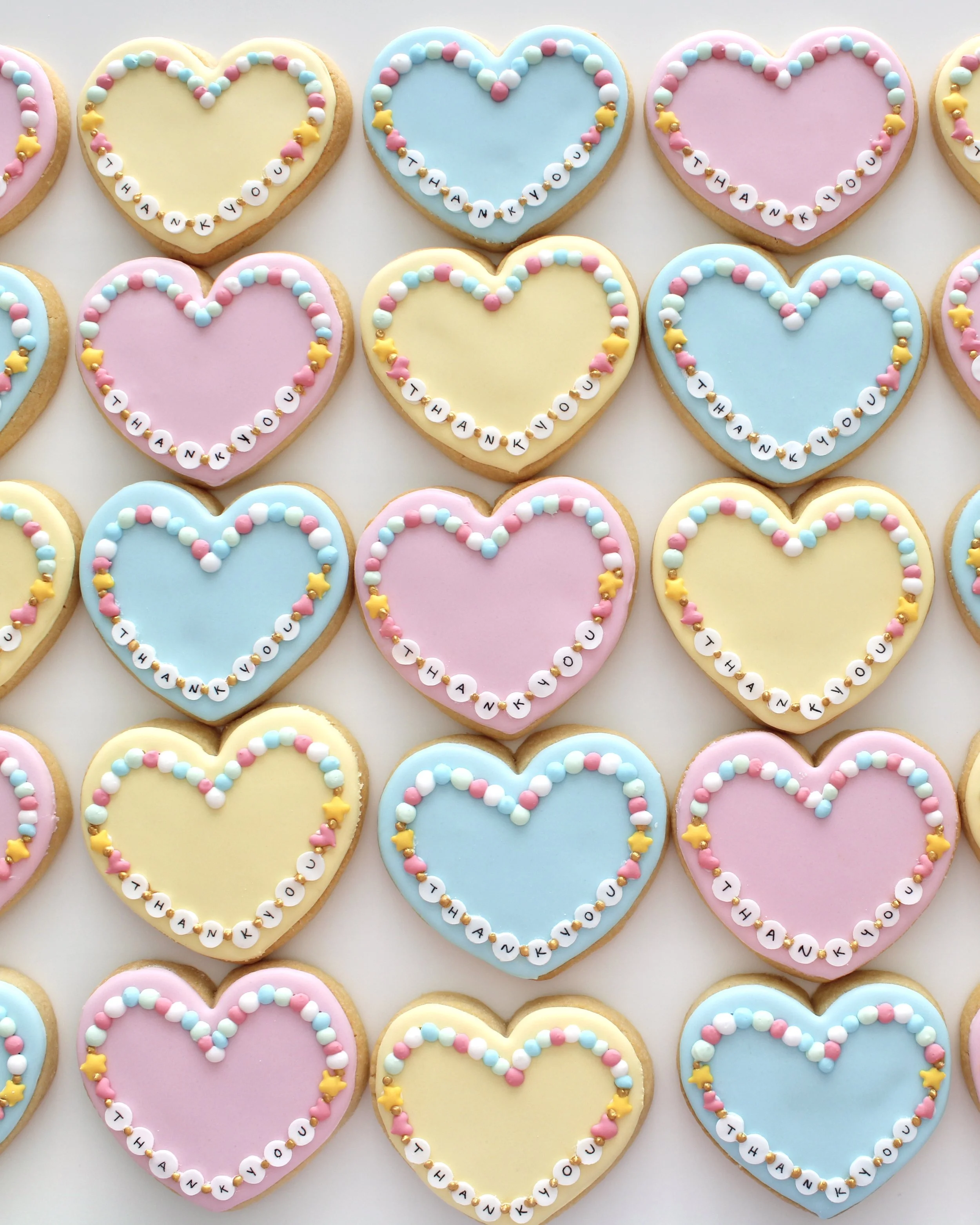 Heart-shaped friendship bracelet cookies in pastel blue, pink, and yellow.