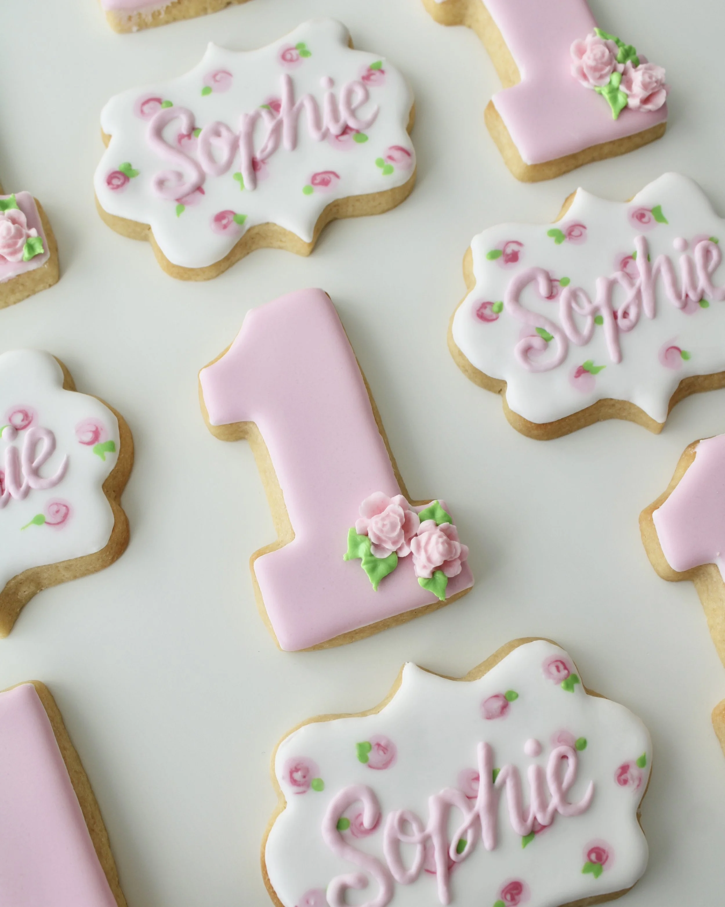Close-up pink number one cookie decorated with delicate piped pink roses and green leaves for a floral first birthday theme.
