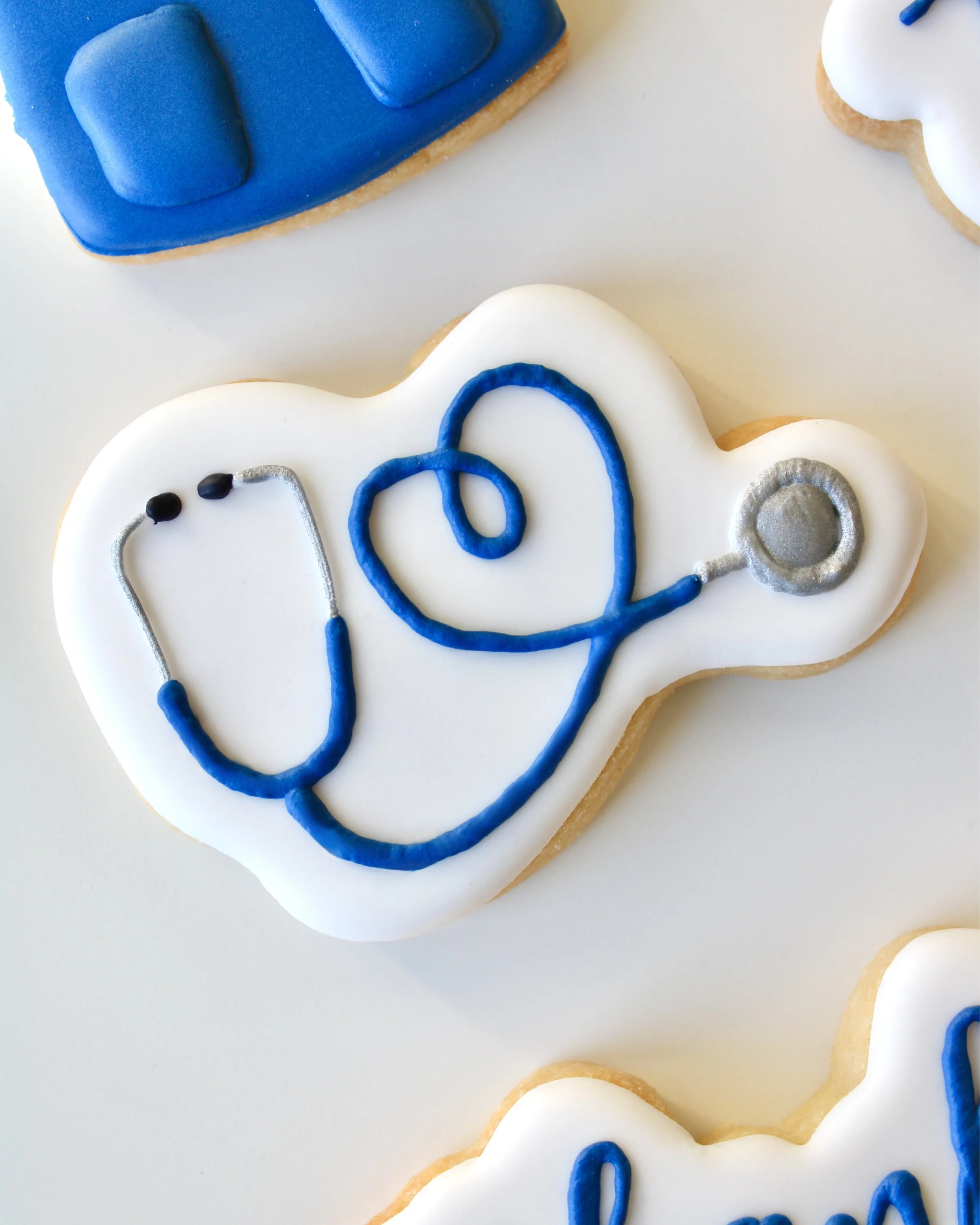 White iced cookie featuring a blue and silver stethoscope looped into a heart shape.