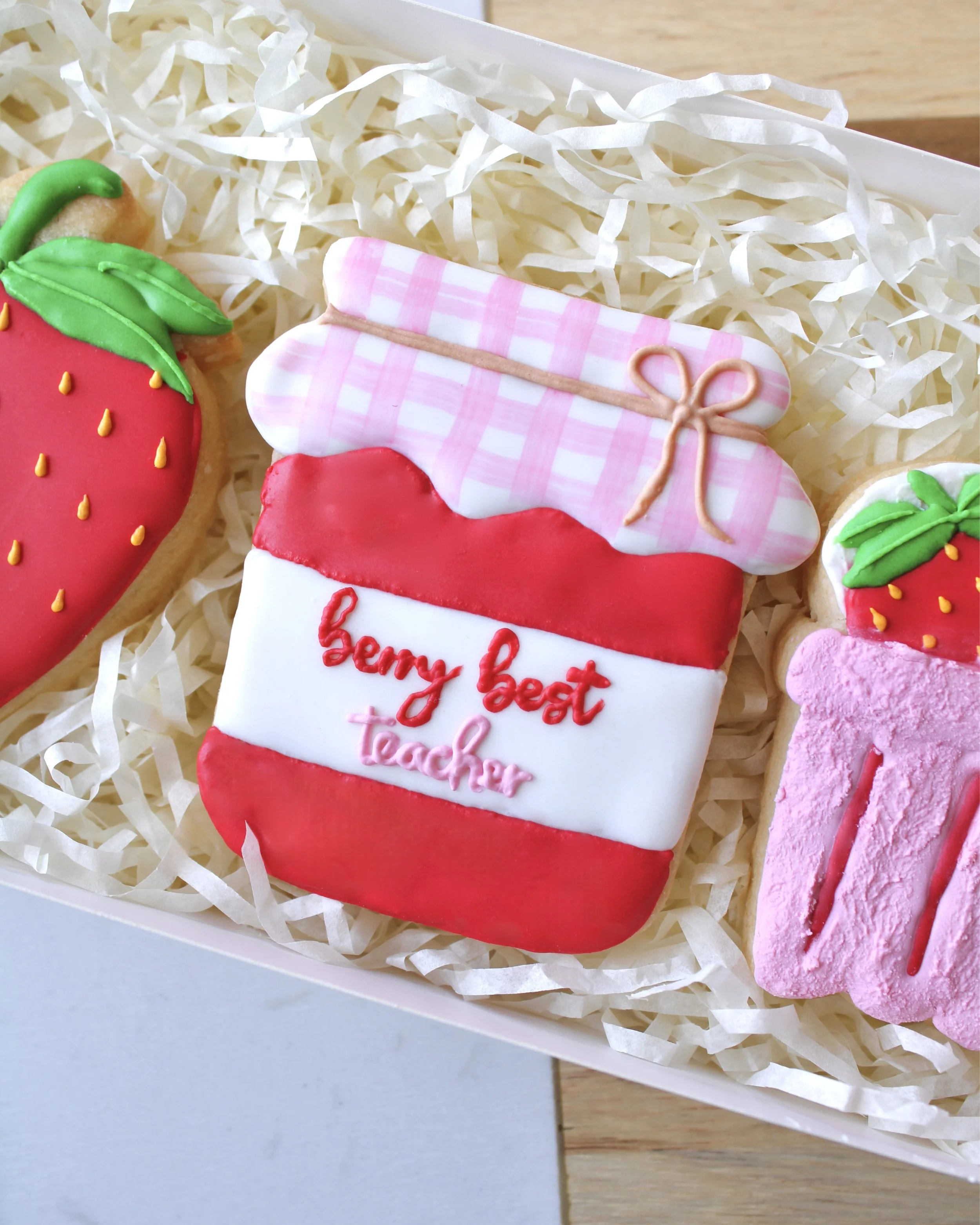 Close-up of a strawberry jam jar cookie labelled “berry best teacher” in red and pink royal icing with a white and pink checkered lid.