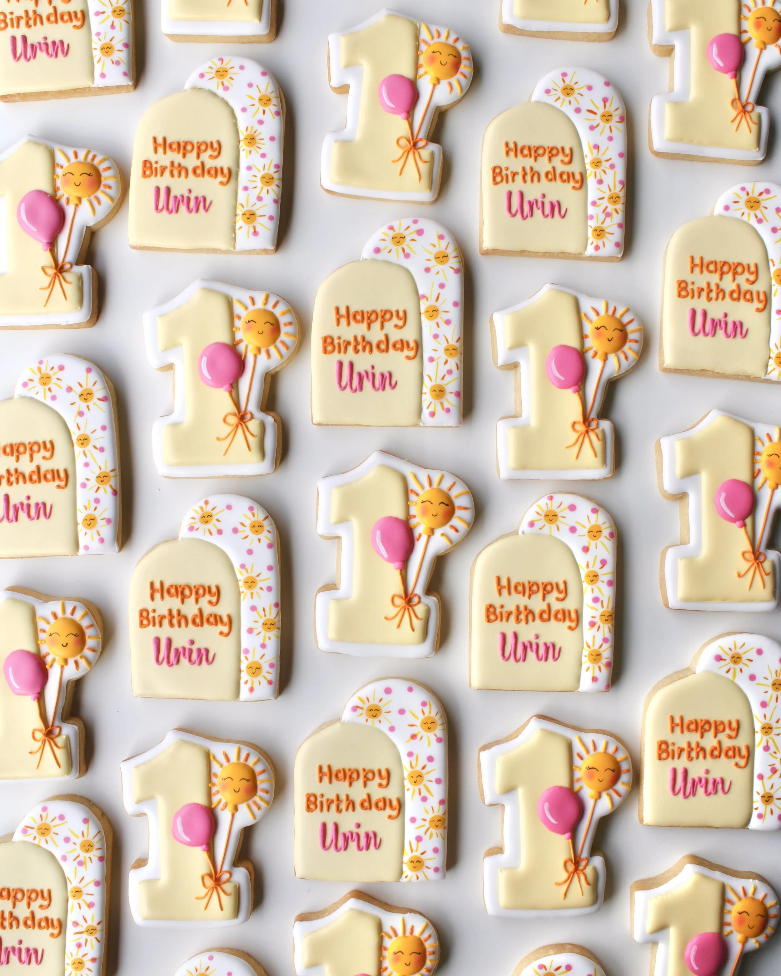 Sunny One themed birthday cookies featuring pale and bright yellows, white, hot pink and orange accents, with double arch designs, hand-painted suns and a number 1 cookie with balloon details.