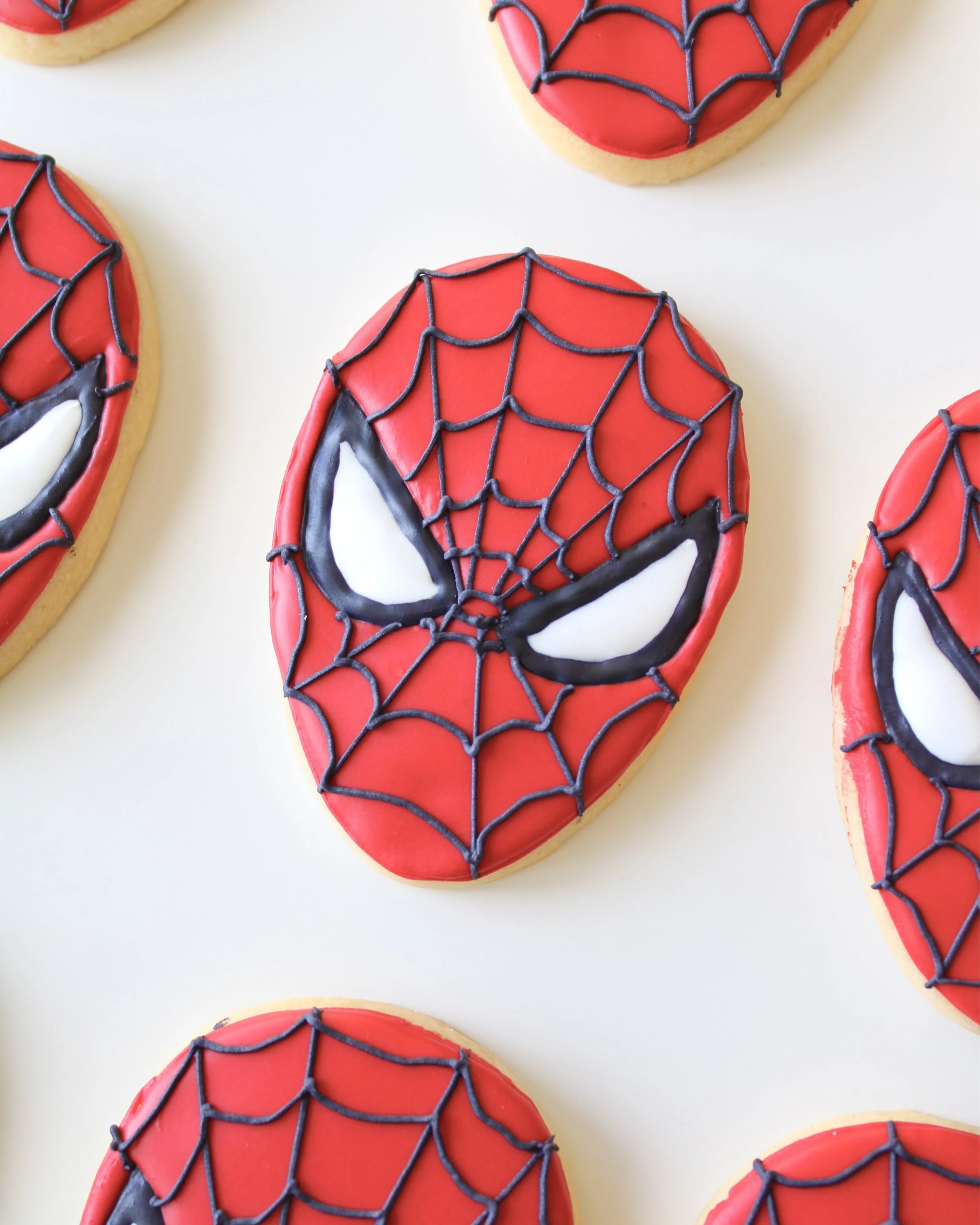 Spiderman themed birthday sugar cookies decorated with red royal icing and black web details