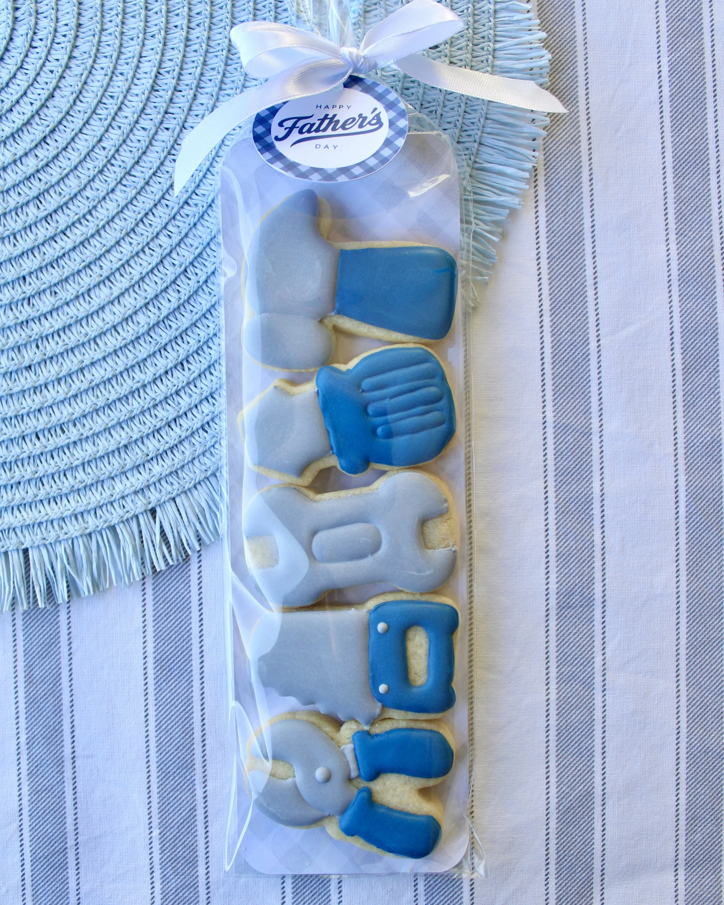 Father’s Day cookie pack with mini tool-shaped sugar cookies including a hammer, screwdriver, wrench, saw and pliers in grey and blue, packaged with a white bow and Happy Father’s Day gift tag.
