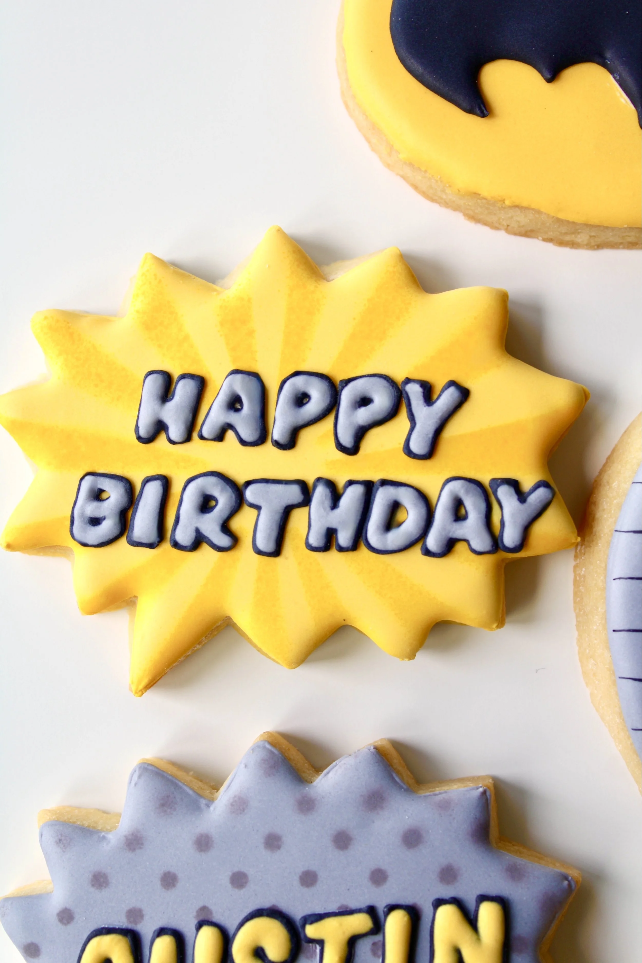 Close-up of yellow and grey speech bubble cookie with “Happy Birthday” in comic-style lettering