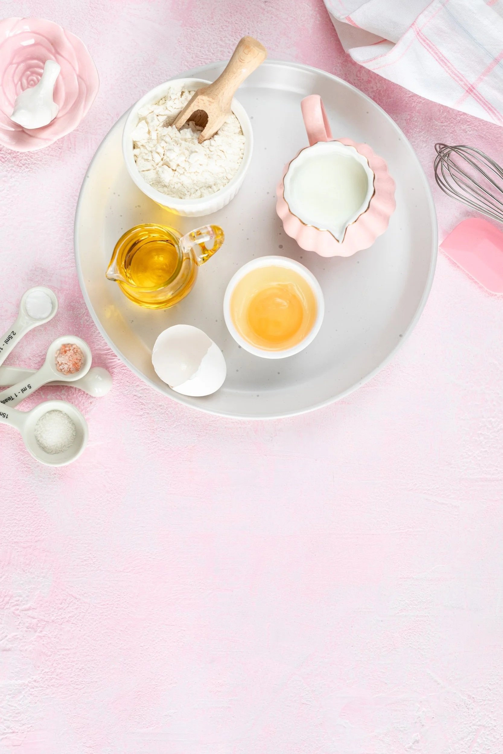 Top view flat lay of baking ingredients and kitchen utensils arranged on a pink background