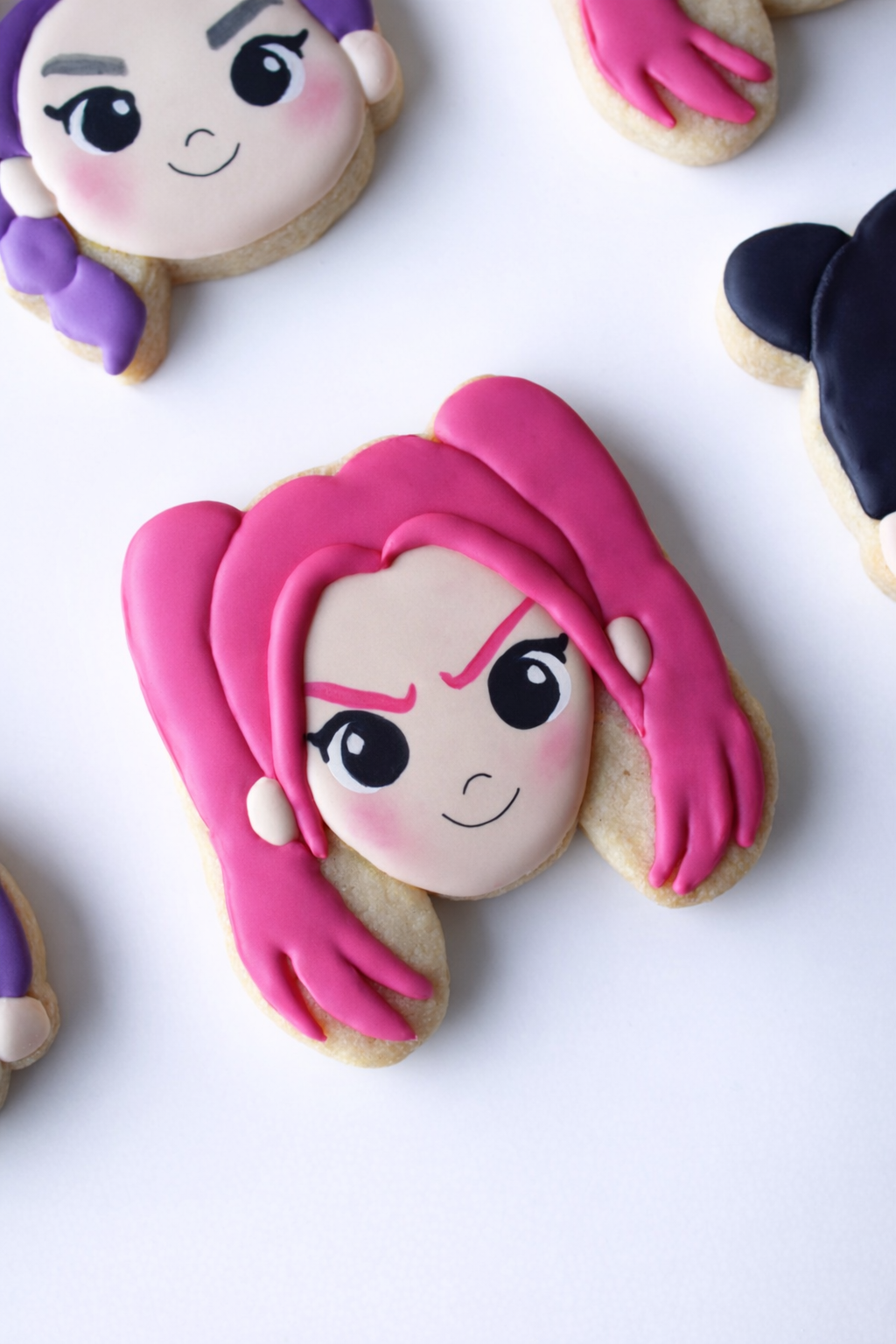 Close-up of a Demon Hunters Huntrix inspired Mira cookie face featuring pink hair, rosy cheeks, and delicate black eyeliner makeup, with a smiling expression on a white background.