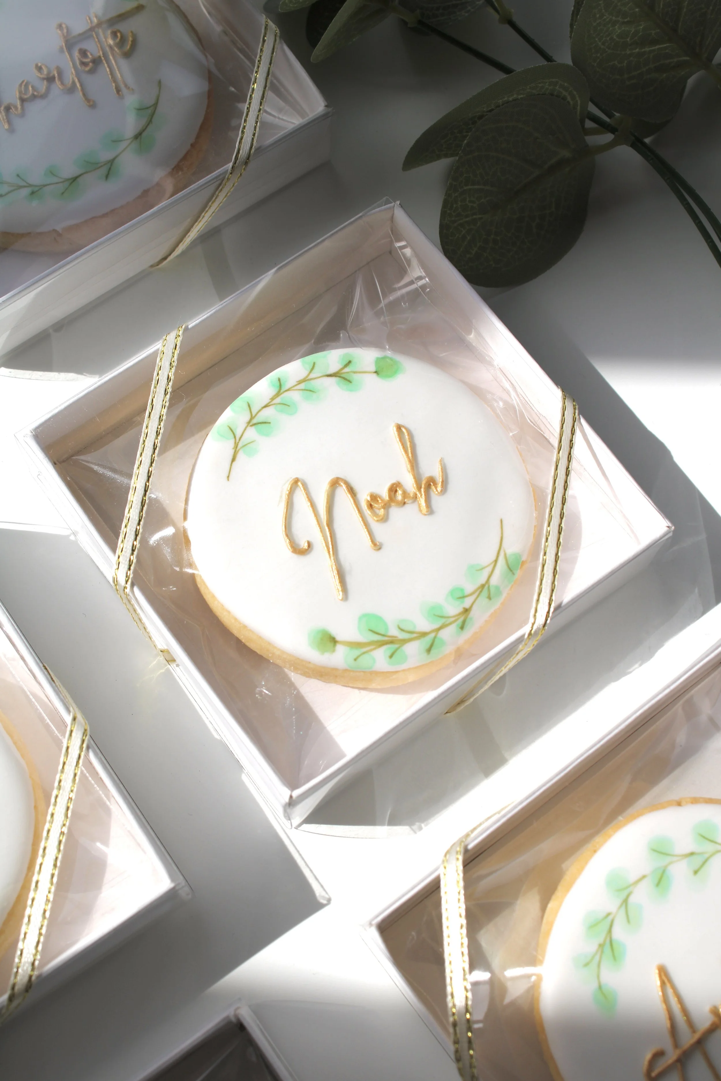 Close-up of a personalised eucalyptus wedding place card cookie with hand-painted watercolour greenery and edible gold name detail