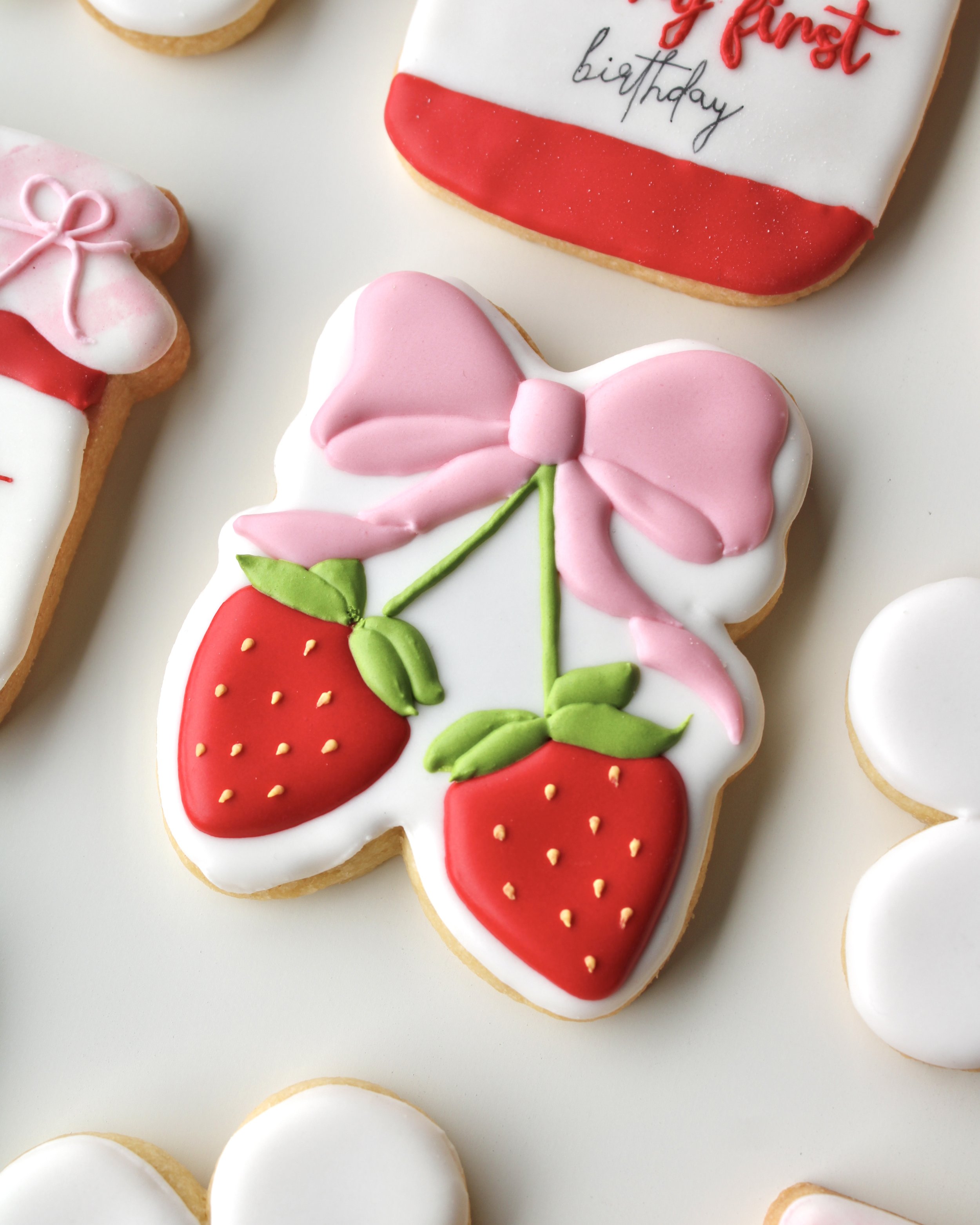 Close-up of cookie featuring two red strawberries tied together with a pink bow.
