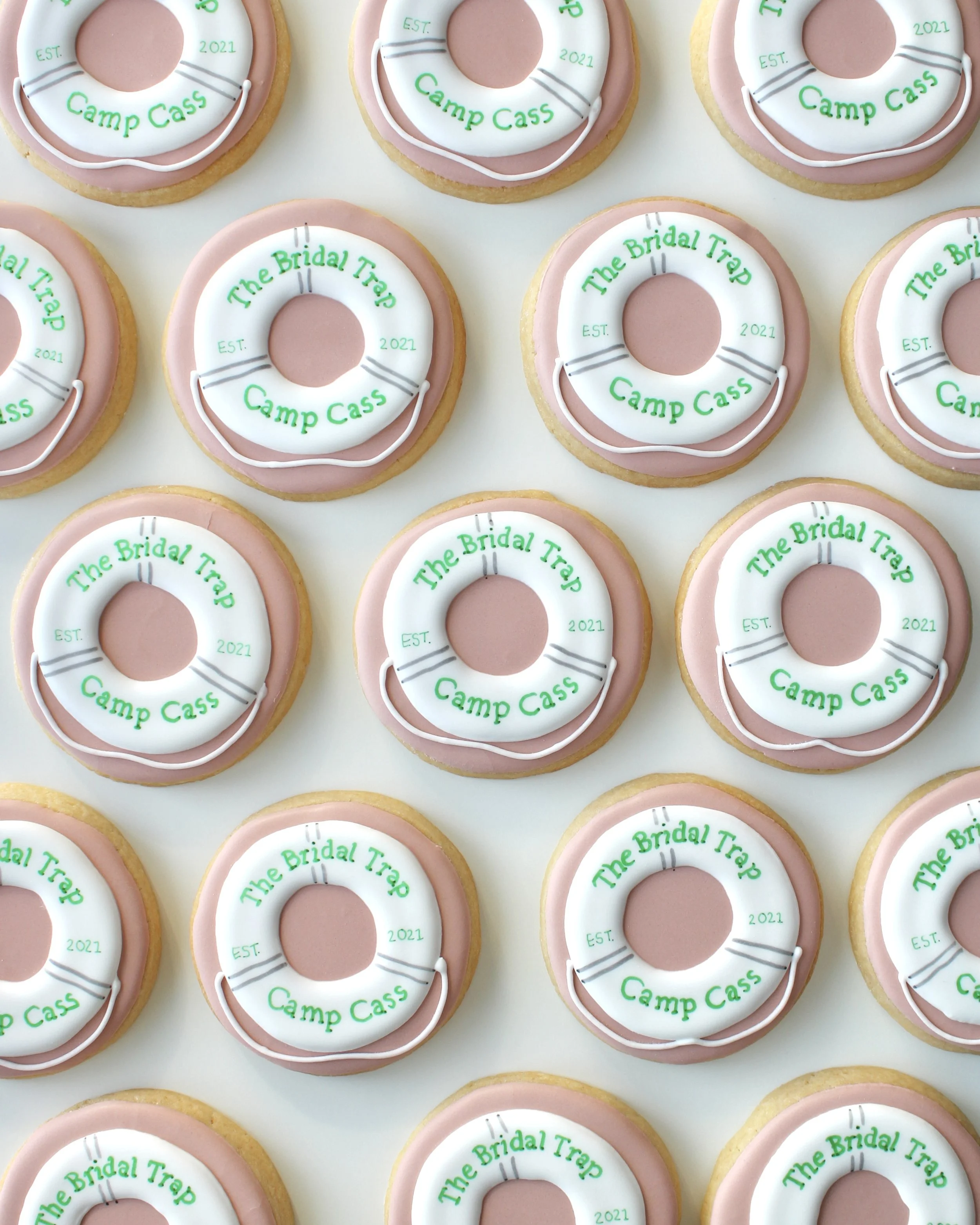 “The Bridal Trap” themed bridal shower cookies featuring a white life buoy on a nude iced cookie with green writing reading “The Bridal Trap, Camp Cass, Est 2021”.