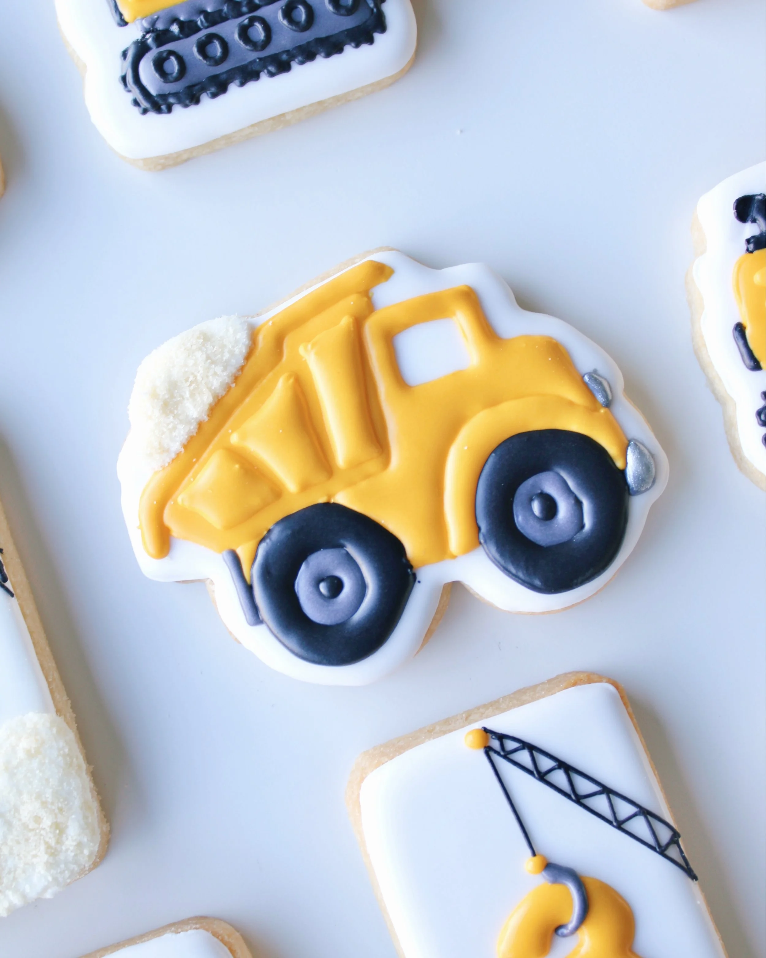 Close-up of a yellow dump truck cookie with sand in the back, black tyres and silver accents.