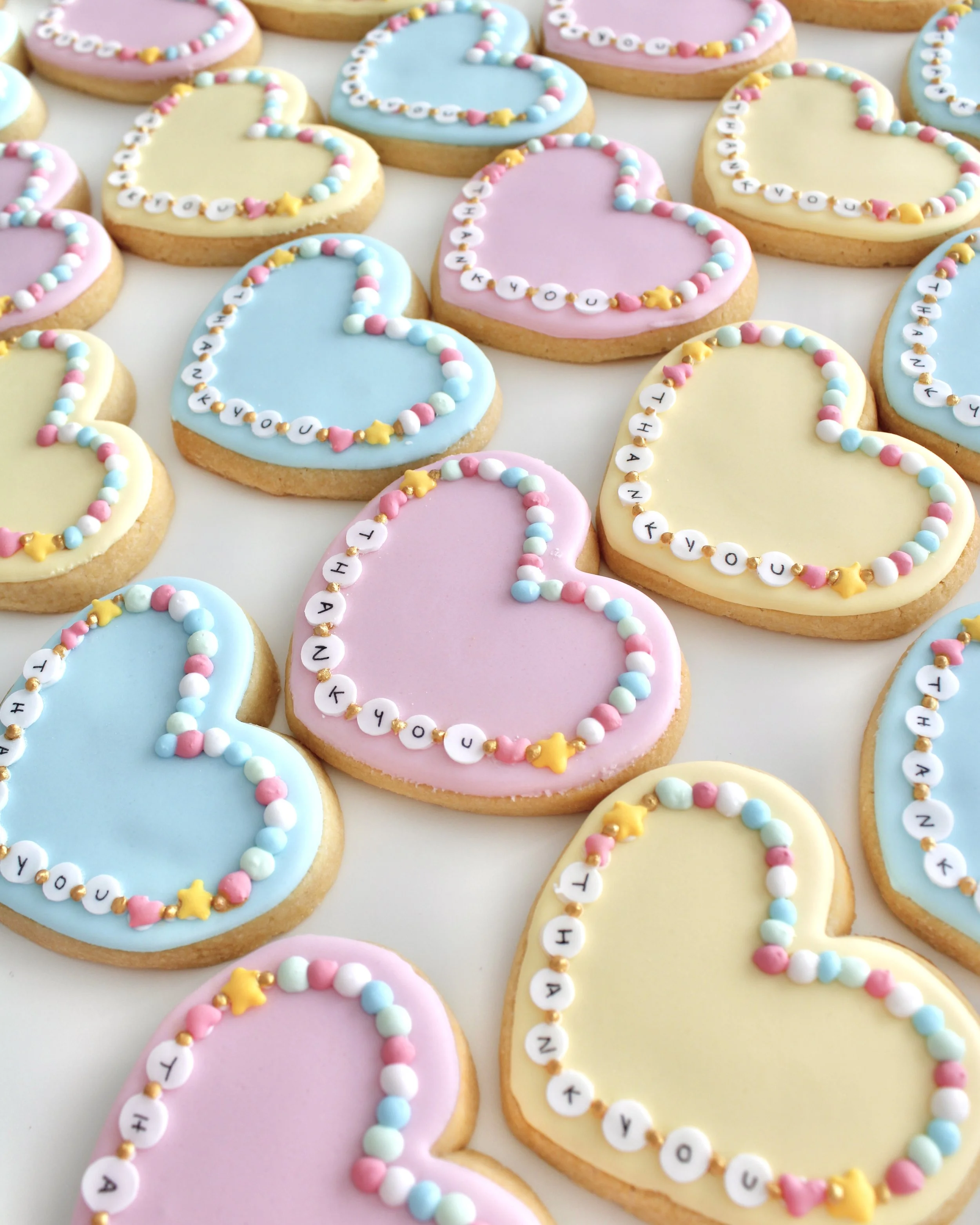Heart-shaped friendship bracelet cookies in pastel blue, pink, and yellow.