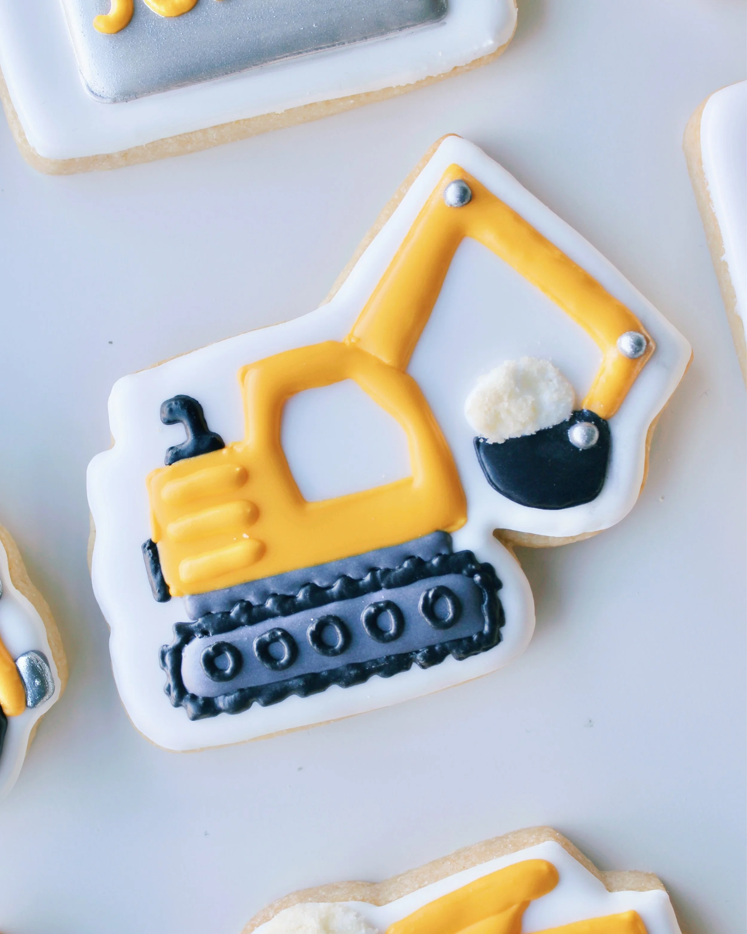 Close-up of a yellow excavator-themed construction cookie with sand in the digger, featuring black and silver accents.