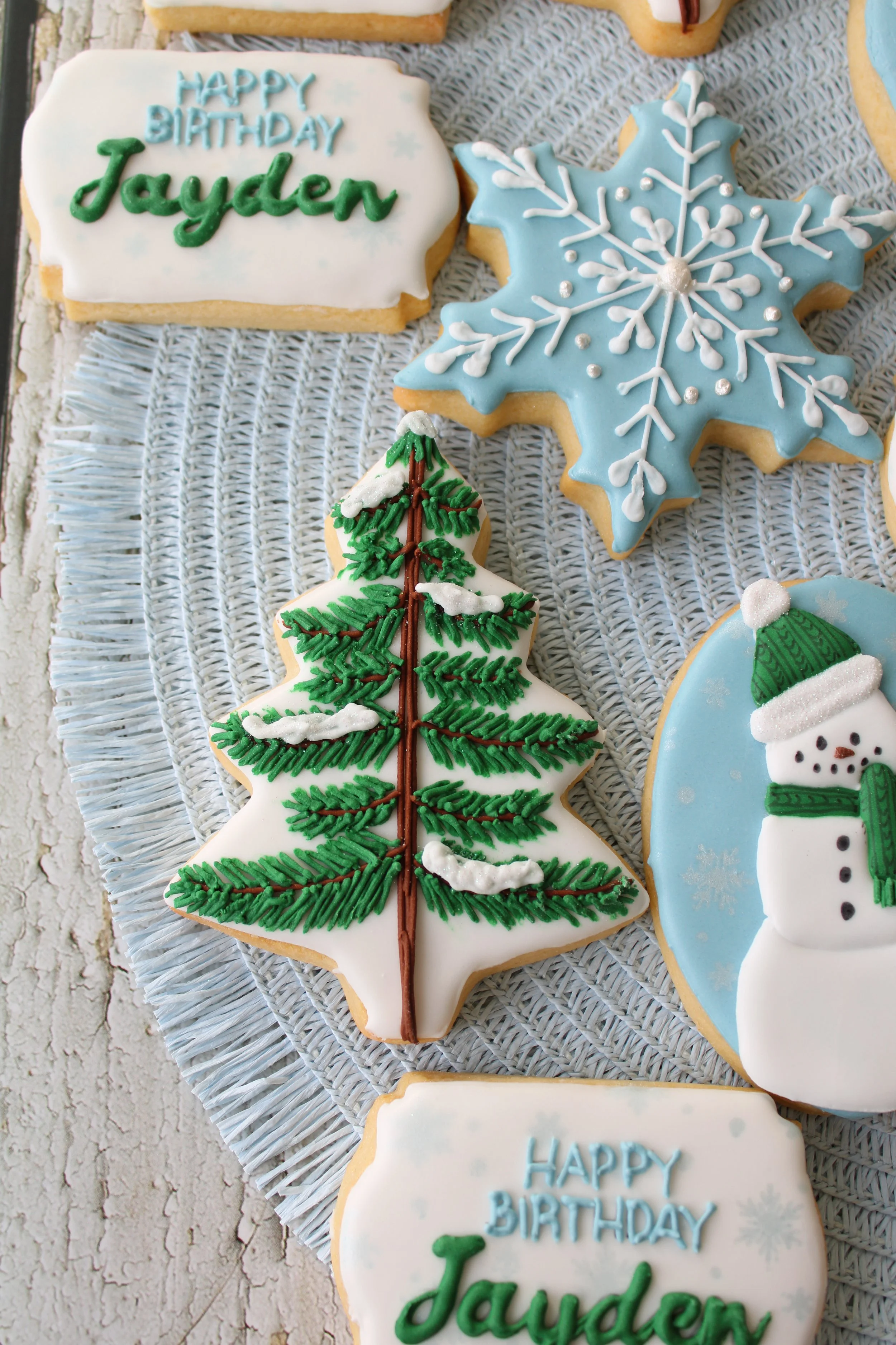 Close-up of a dark green pine tree cookie decorated with snow details, styled on a pale blue placemat.