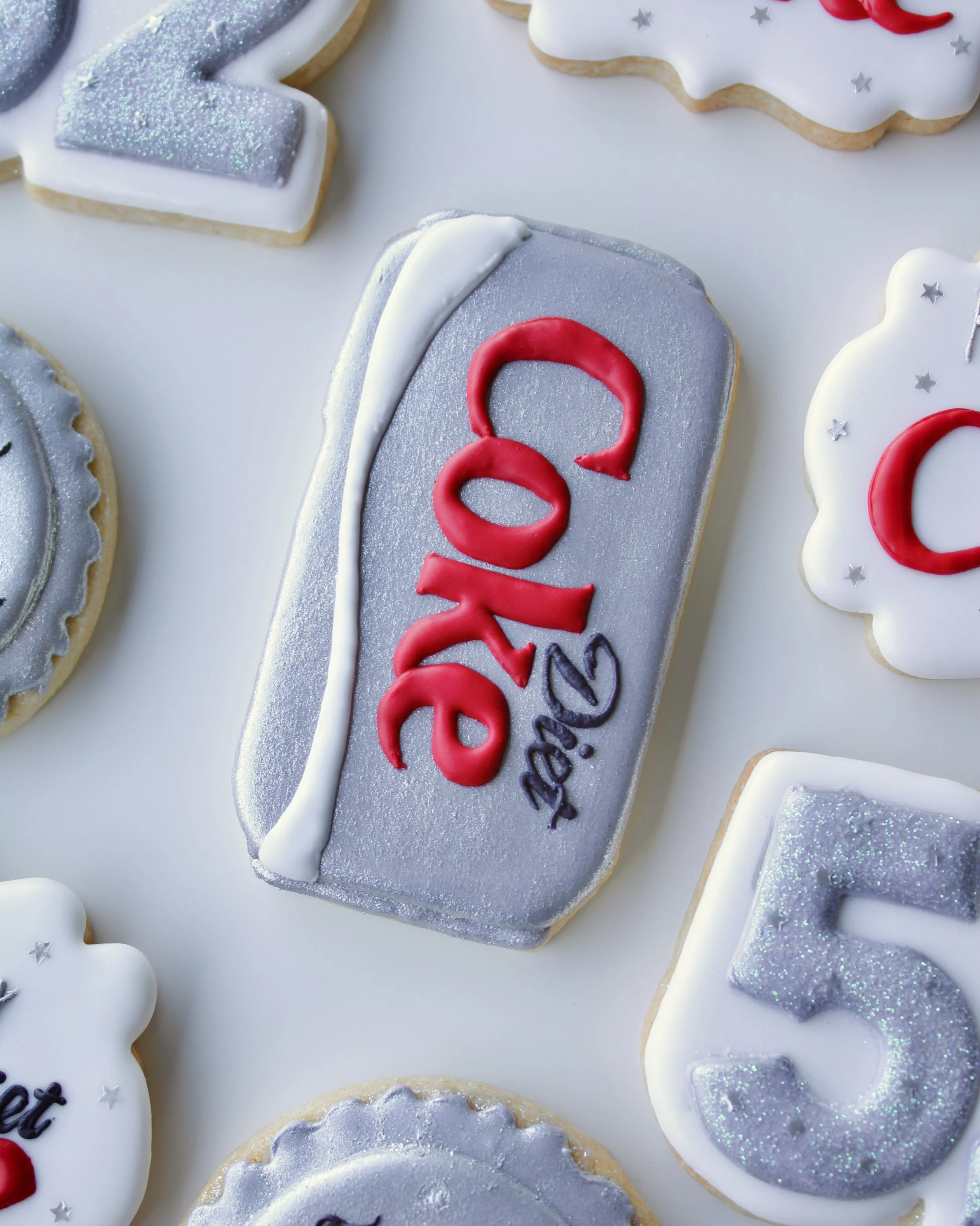 Close-up of a Diet Coke can cookie painted with silver edible paint, featuring red, white and black icing accents.