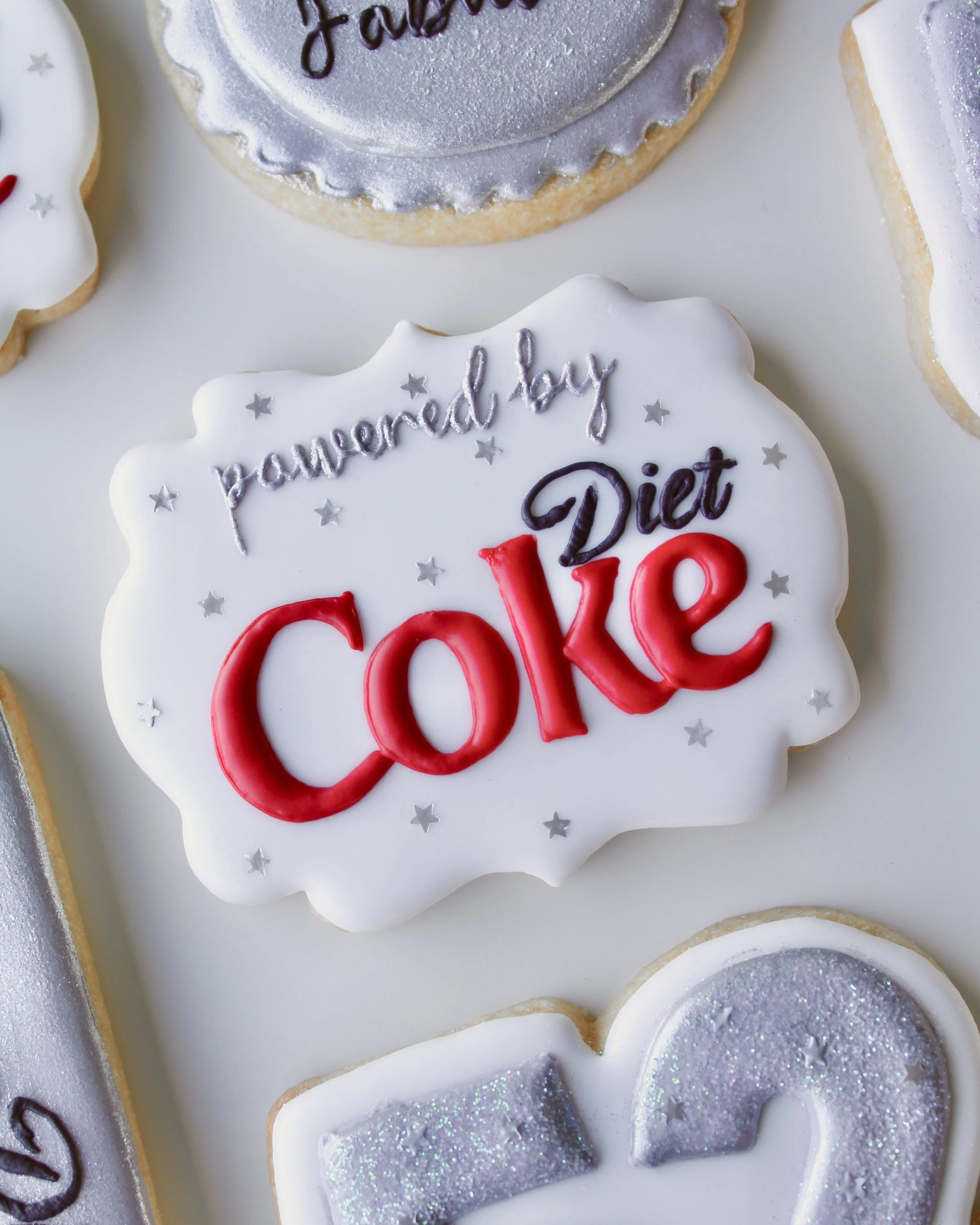 Close-up of a “Powered by Diet Coke” plaque cookie with silver star accents and red, white and black icing details.