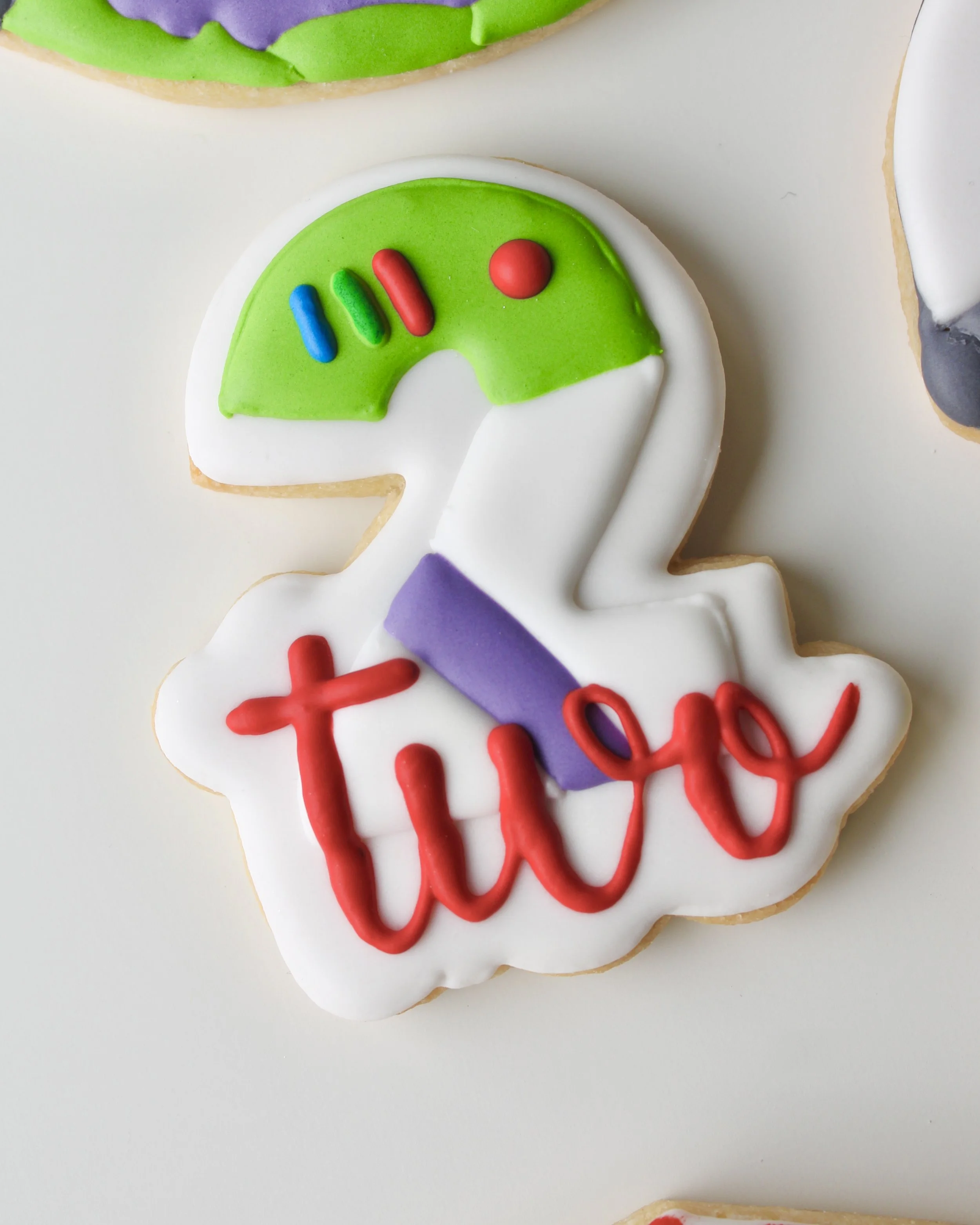 Close-up of a number two royal icing cookie decorated in Buzz Lightyear-inspired colours.