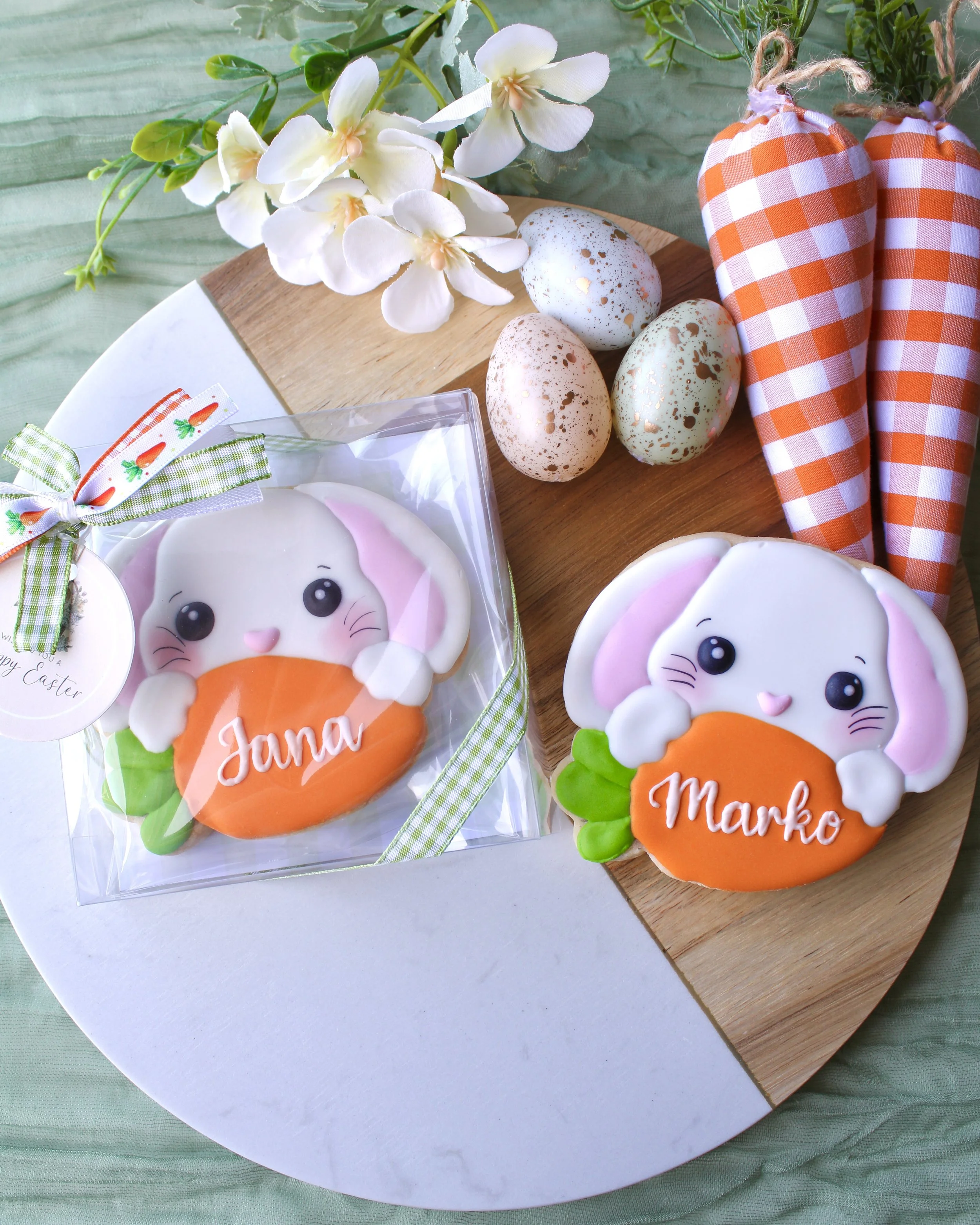 Two personalised Easter bunny sugar cookies in gift boxes with “Jana” and “Marko,” Happy Easter tags and gingham bows, styled on wood and marble board with eggs and spring flowers.