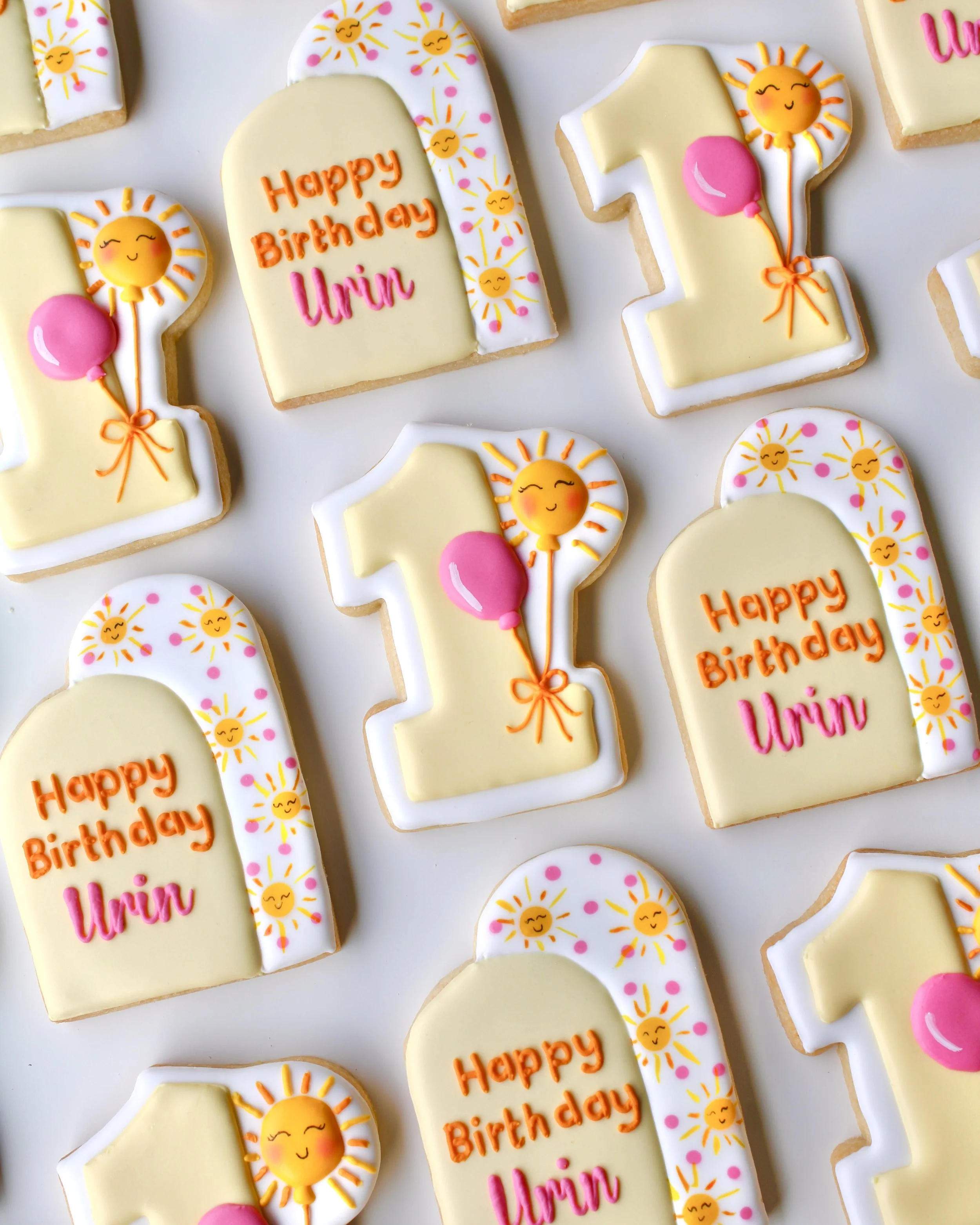 Sunny One themed birthday cookies featuring pale and bright yellows, white, hot pink and orange accents, with double arch designs, hand-painted suns and a number 1 cookie with balloon details.
