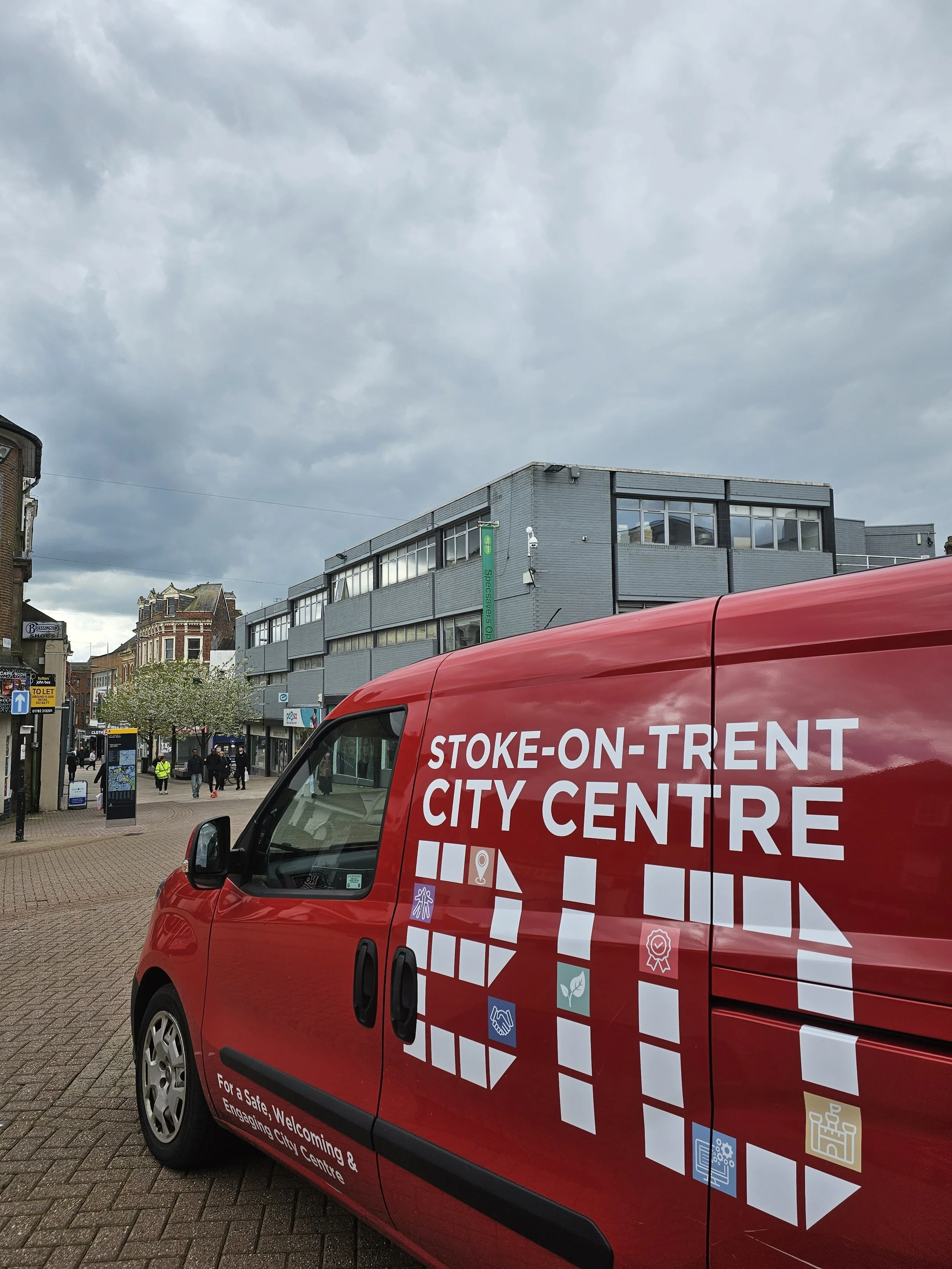 Red city service van parked in front of a modern building with large windows on a cloudy day in Stoke-on-Trent.