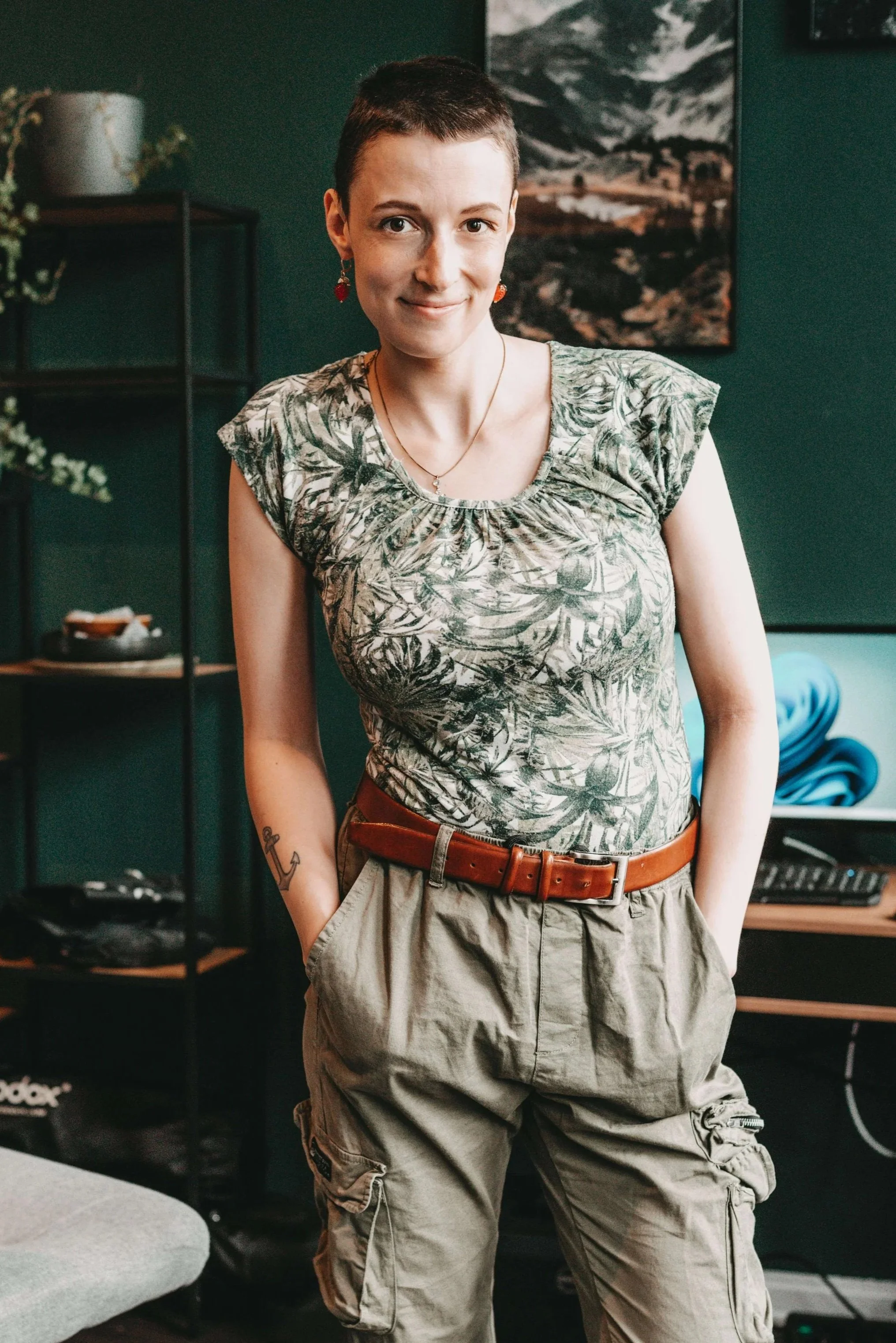 Junge Frau mit kurzen Haare, steht in einem Raum mit grünen Wänden, Blick direkt zur Kamera.