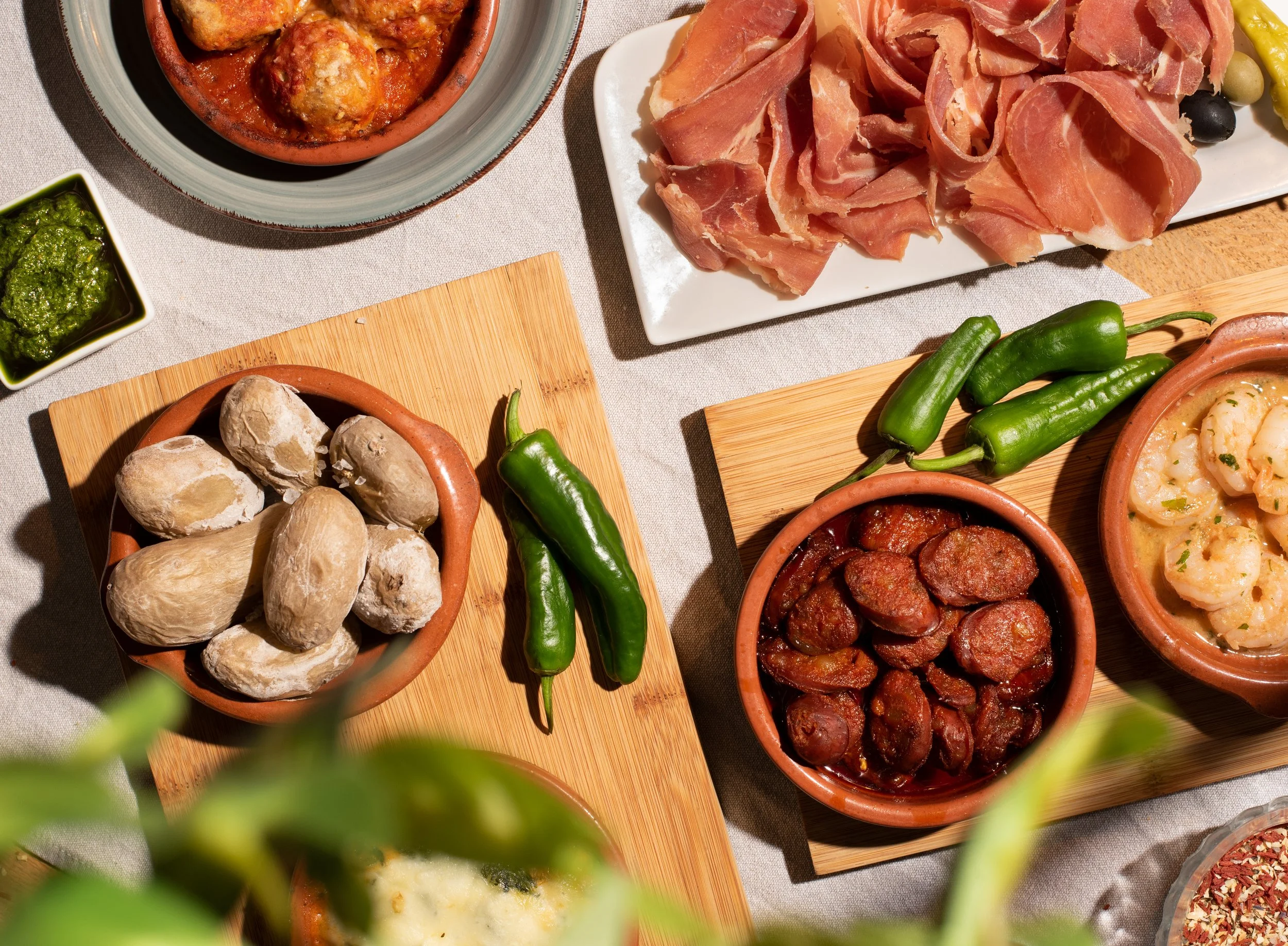 Verschiedene spanische Tapas, darunter Schinken, Oliven, Fleischbällchen und Knoblauchbrot, auf einem gedeckten Tisch.