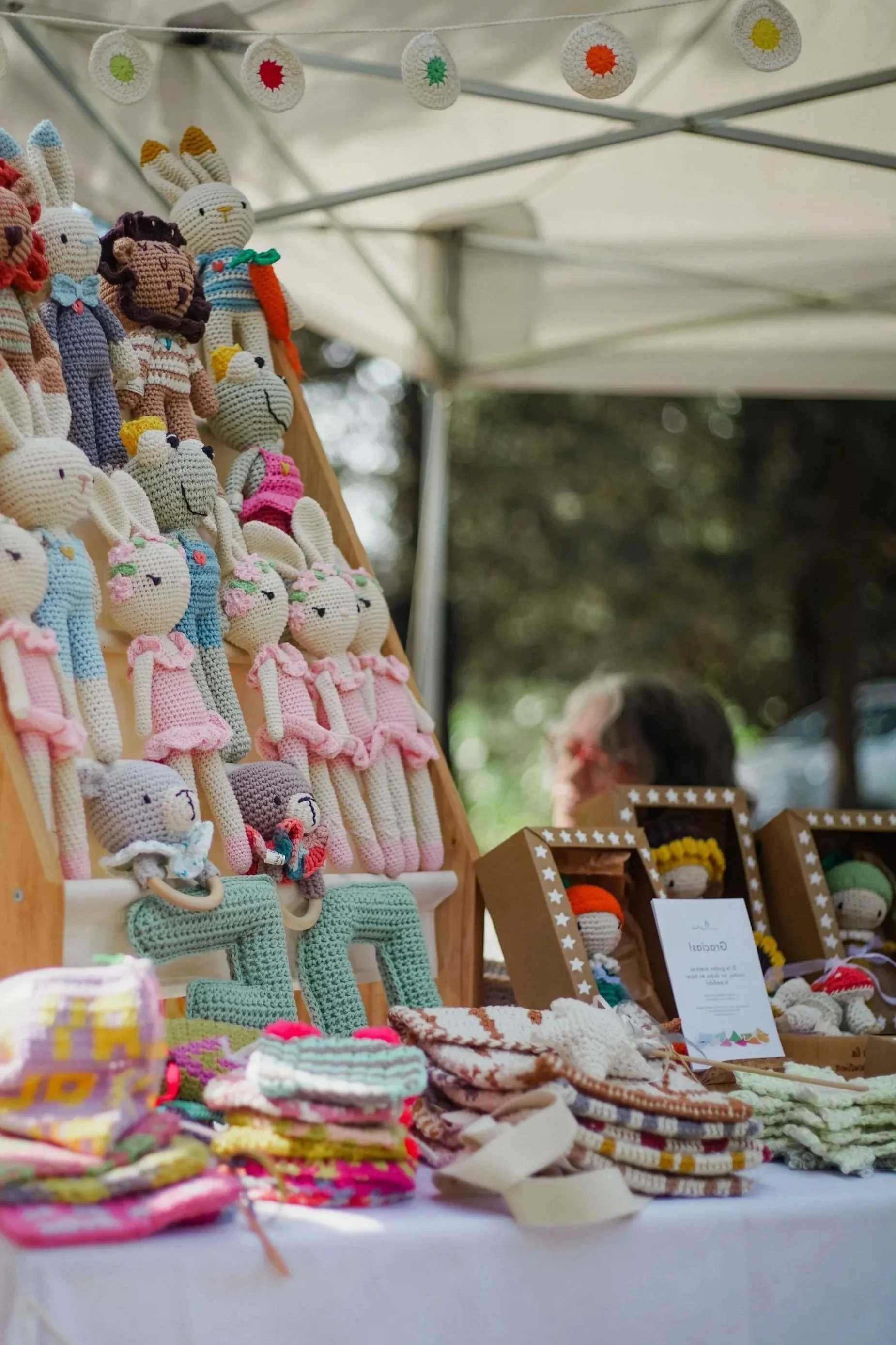Häkeltiere und handgemachte Stoffe auf einem Marktstand, mit bunten Strickwaren und kleinen Dekorationsartikeln.