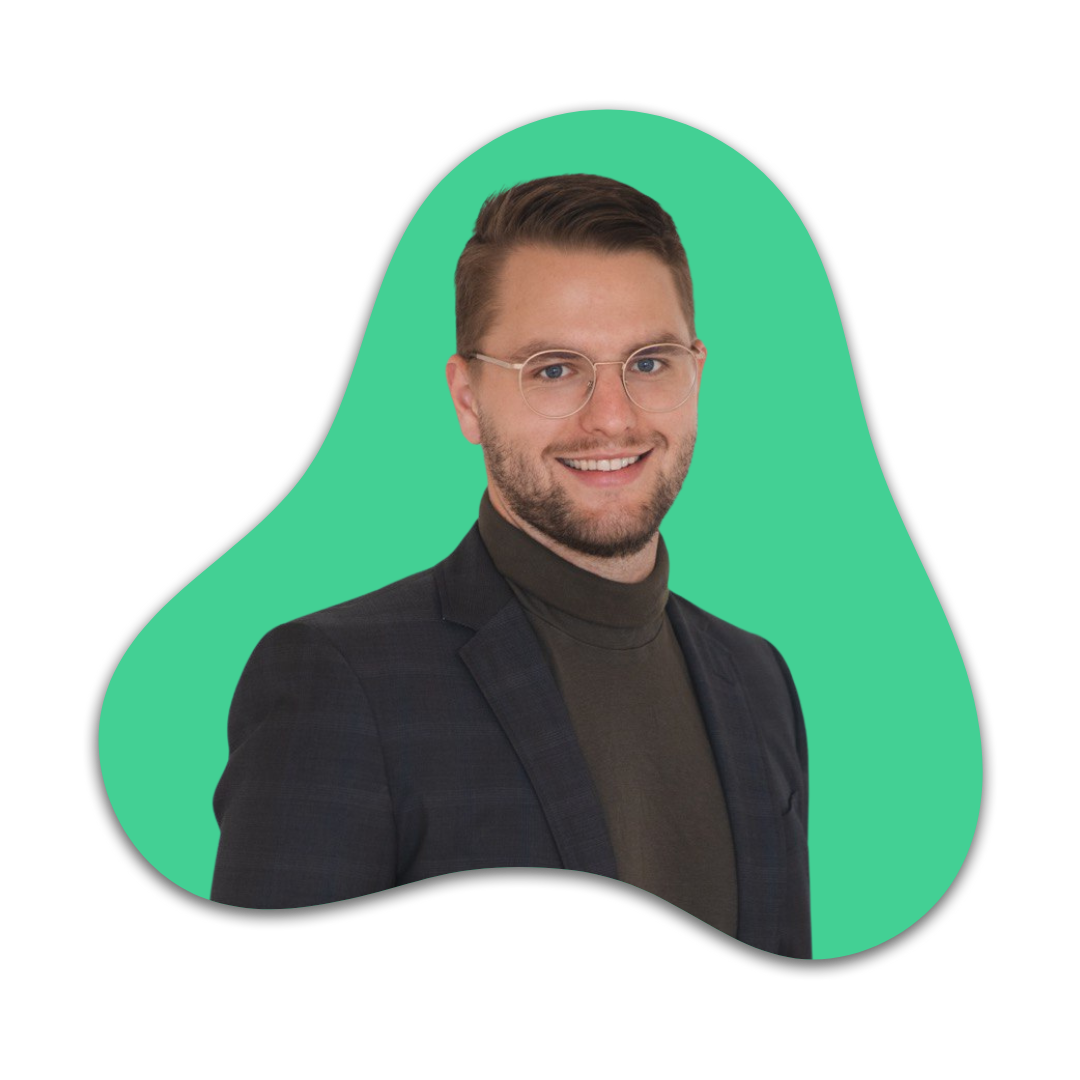 Ein Mann trägt eine schwarze Jacke, einen schwarzen Rollkragen Pullover, Brille und hat braune kurze Haare. Er lächelt und steht vor einem grünen Hintergrund.